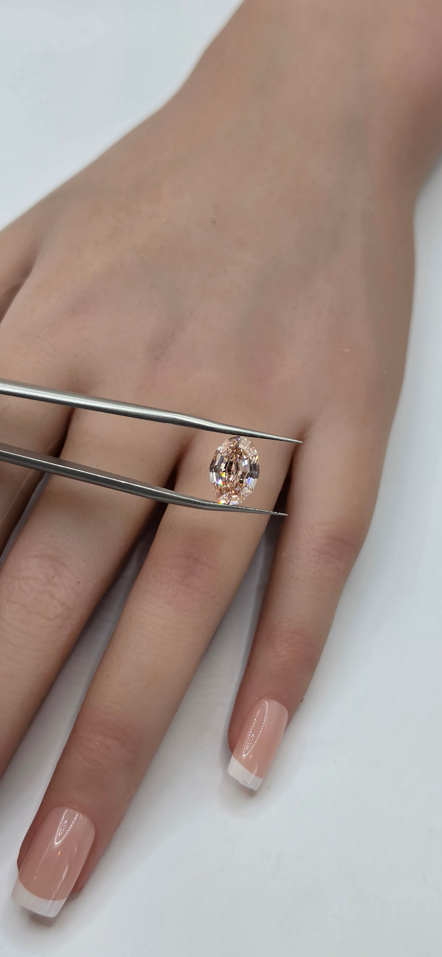 Close-up of a hand wearing a ring with tweezers adjusting it on a white background