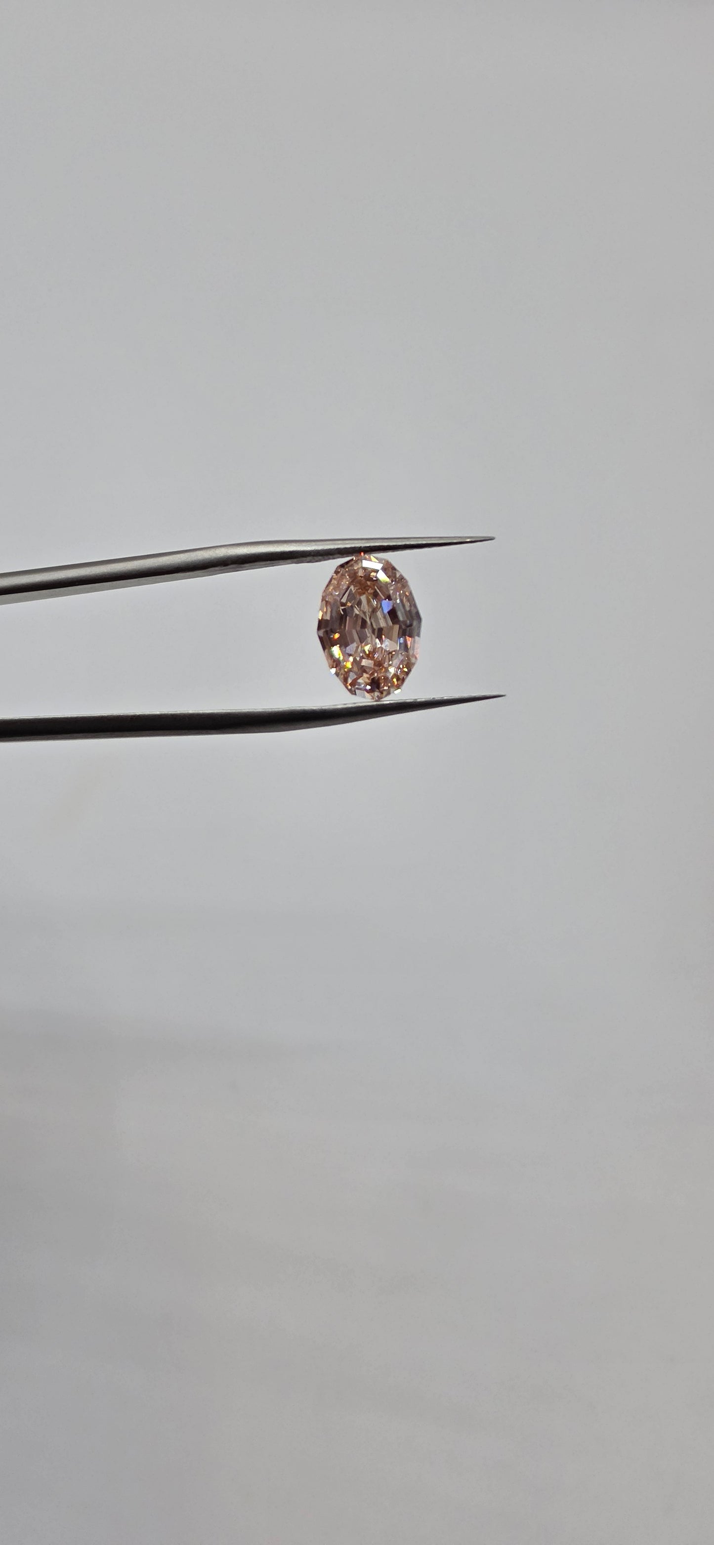 Diamond held between tweezers against a gray background