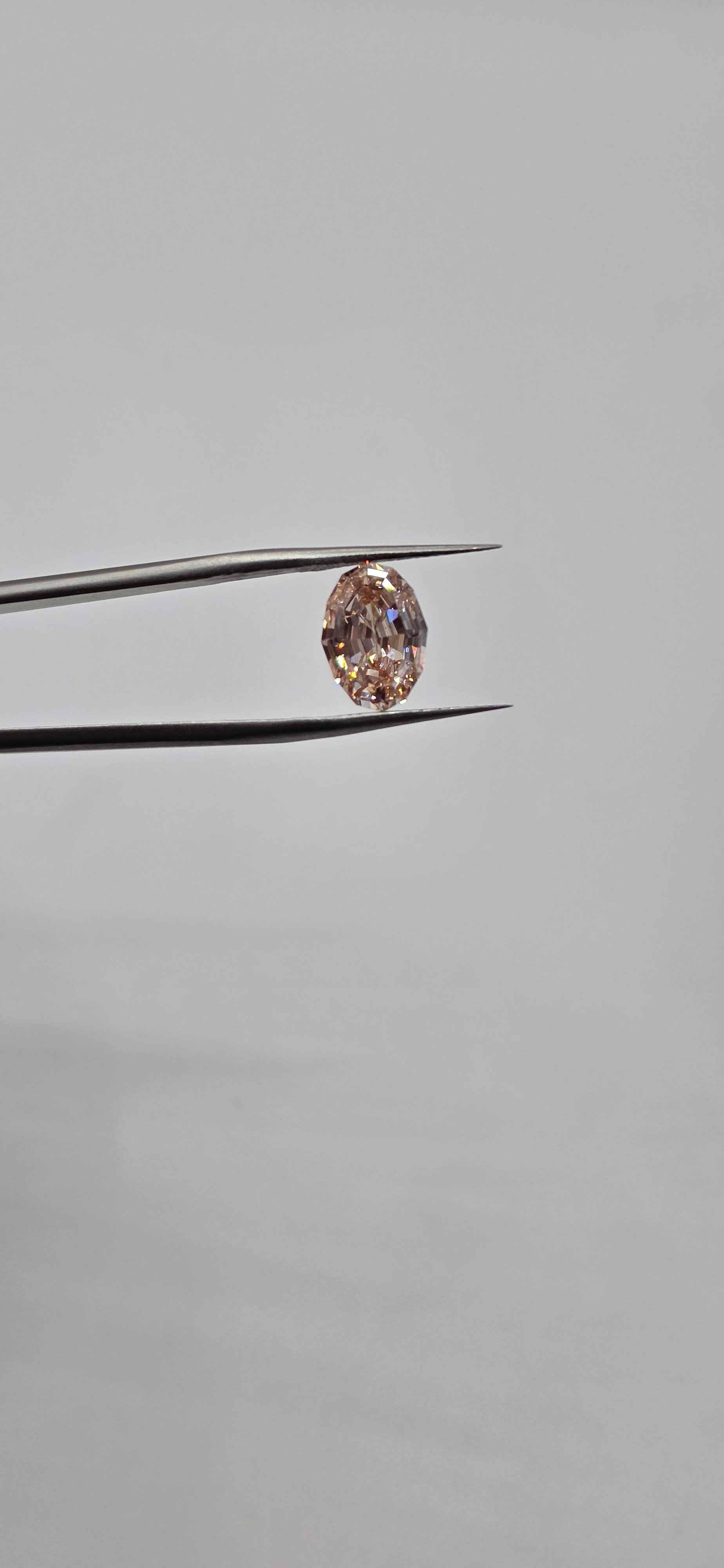 Diamond held between tweezers against a gray background
