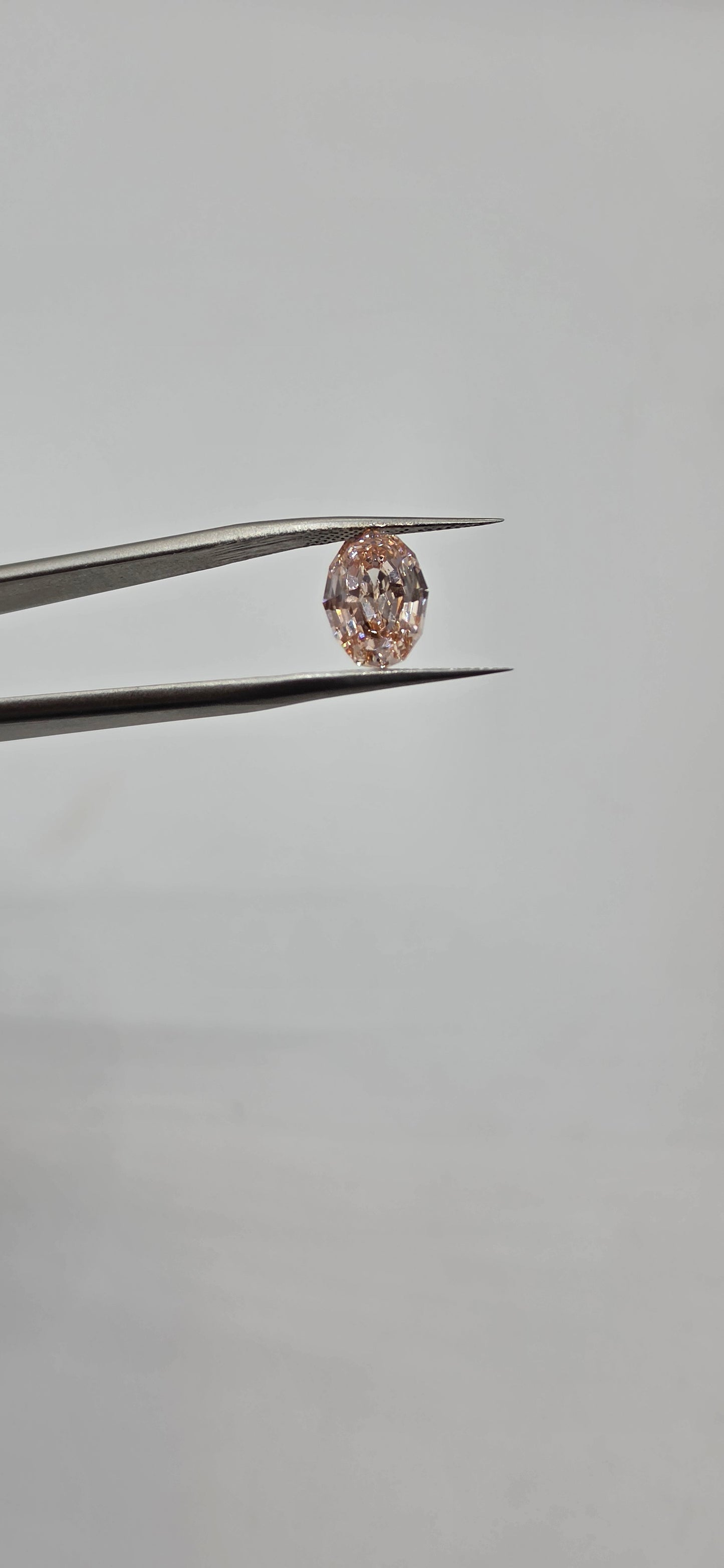 Diamond held between tweezers against a gray background