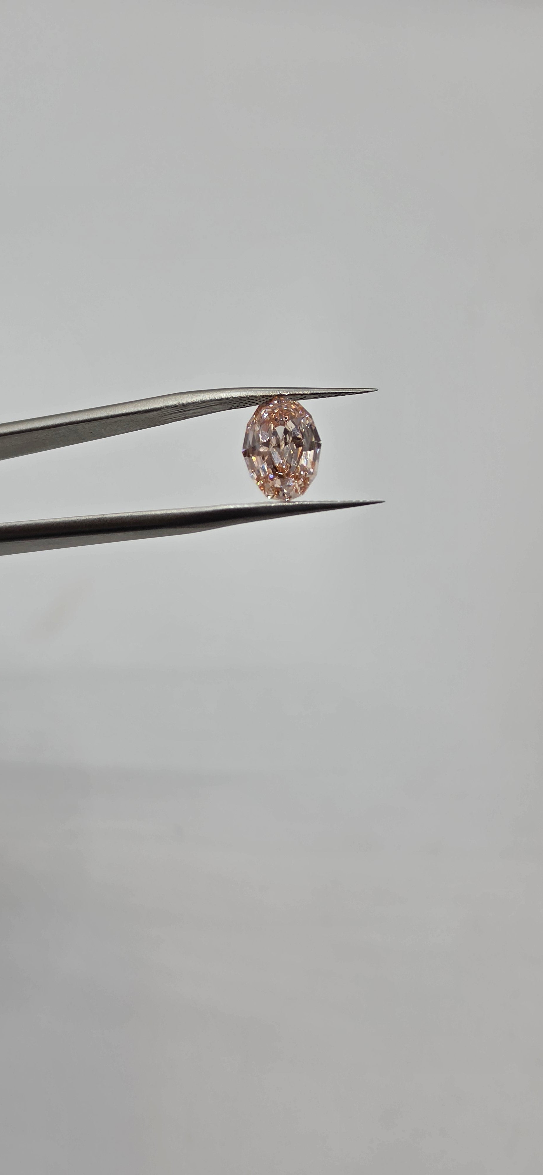 Diamond held between tweezers against a gray background