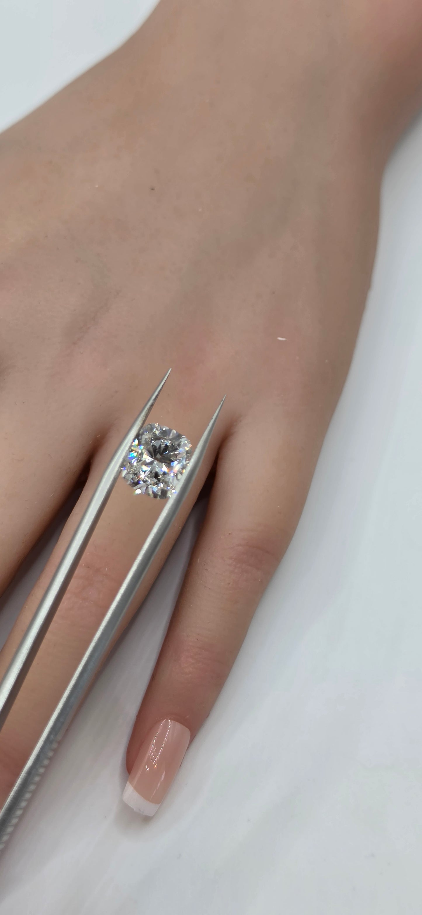 Diamond being held with tweezers against a hand on a white background
