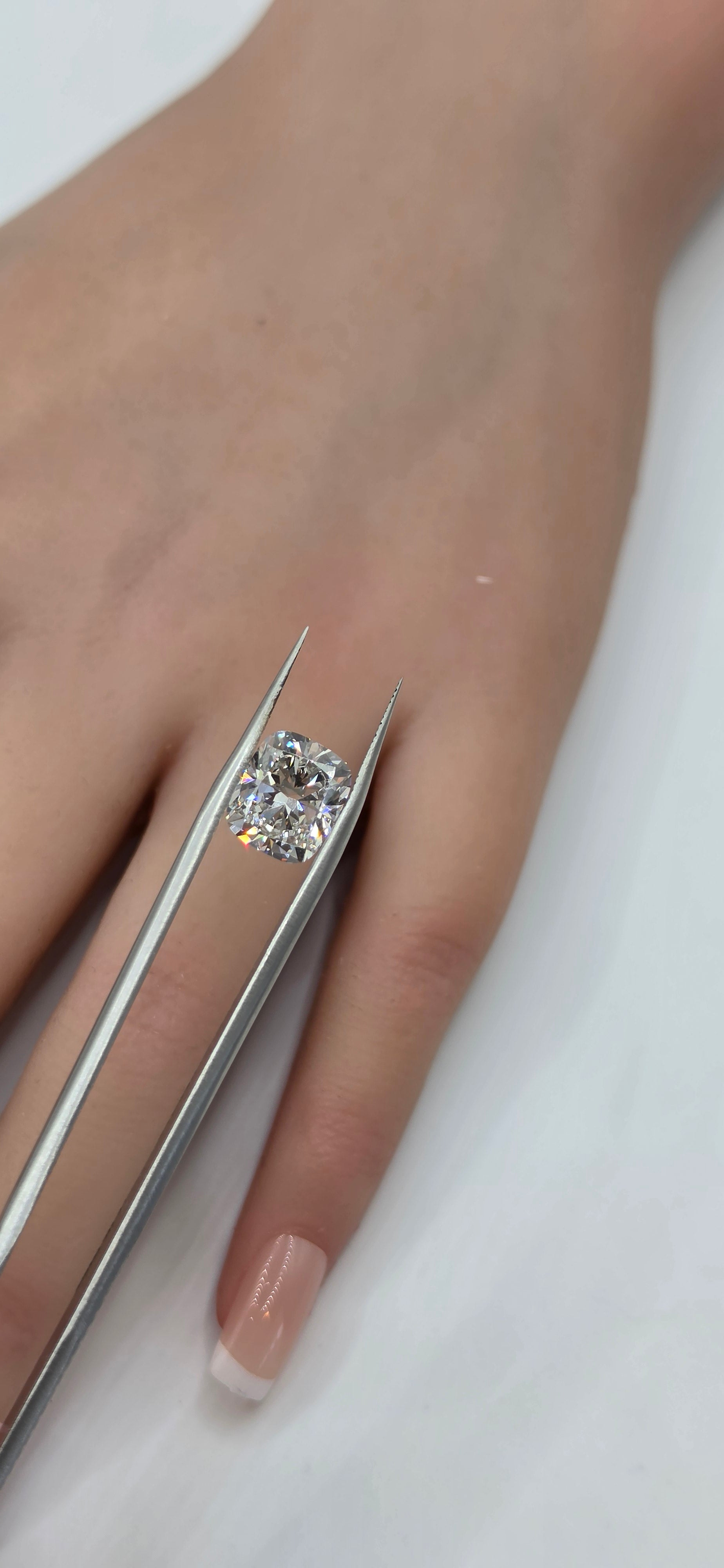 Diamond being held by tweezers against a hand on a white background