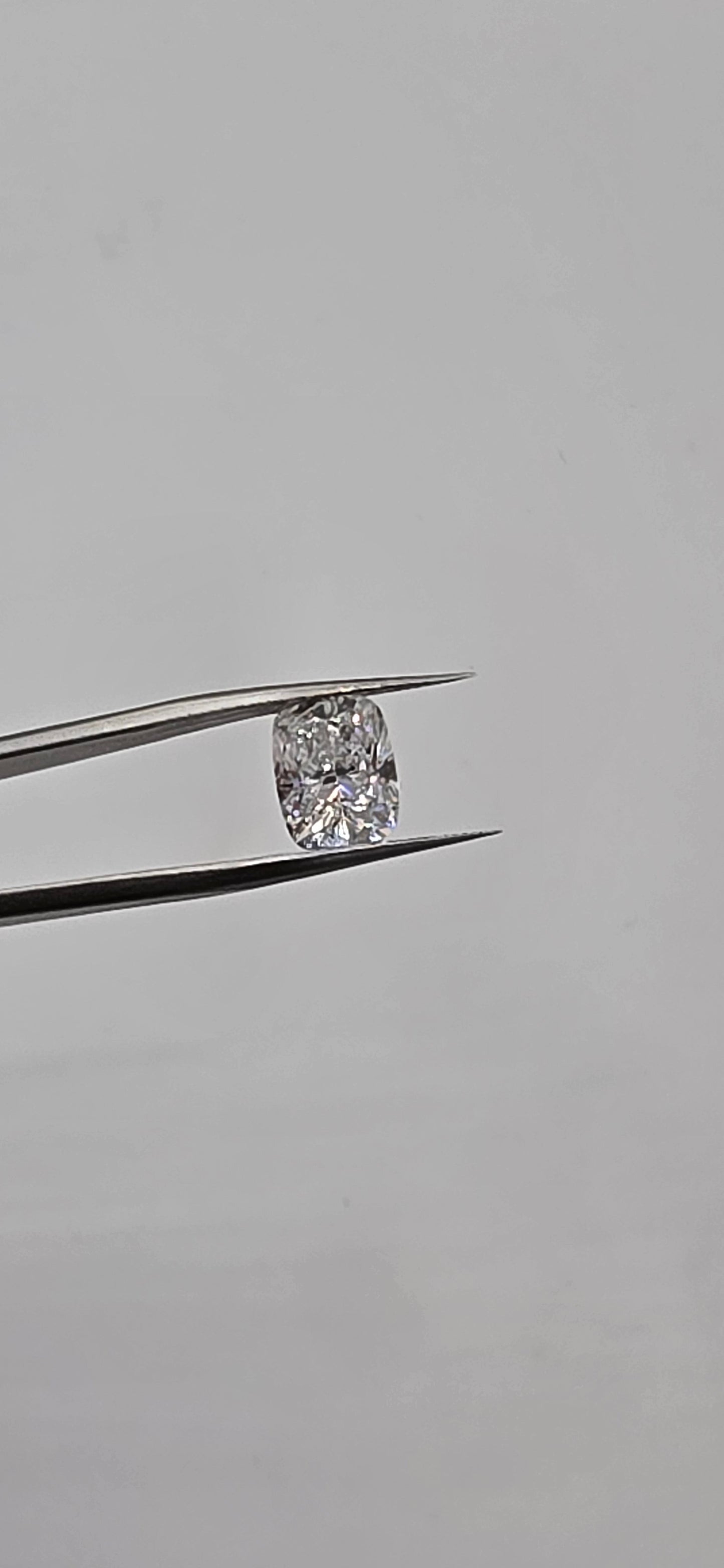 Diamond held between tweezers against a gray background