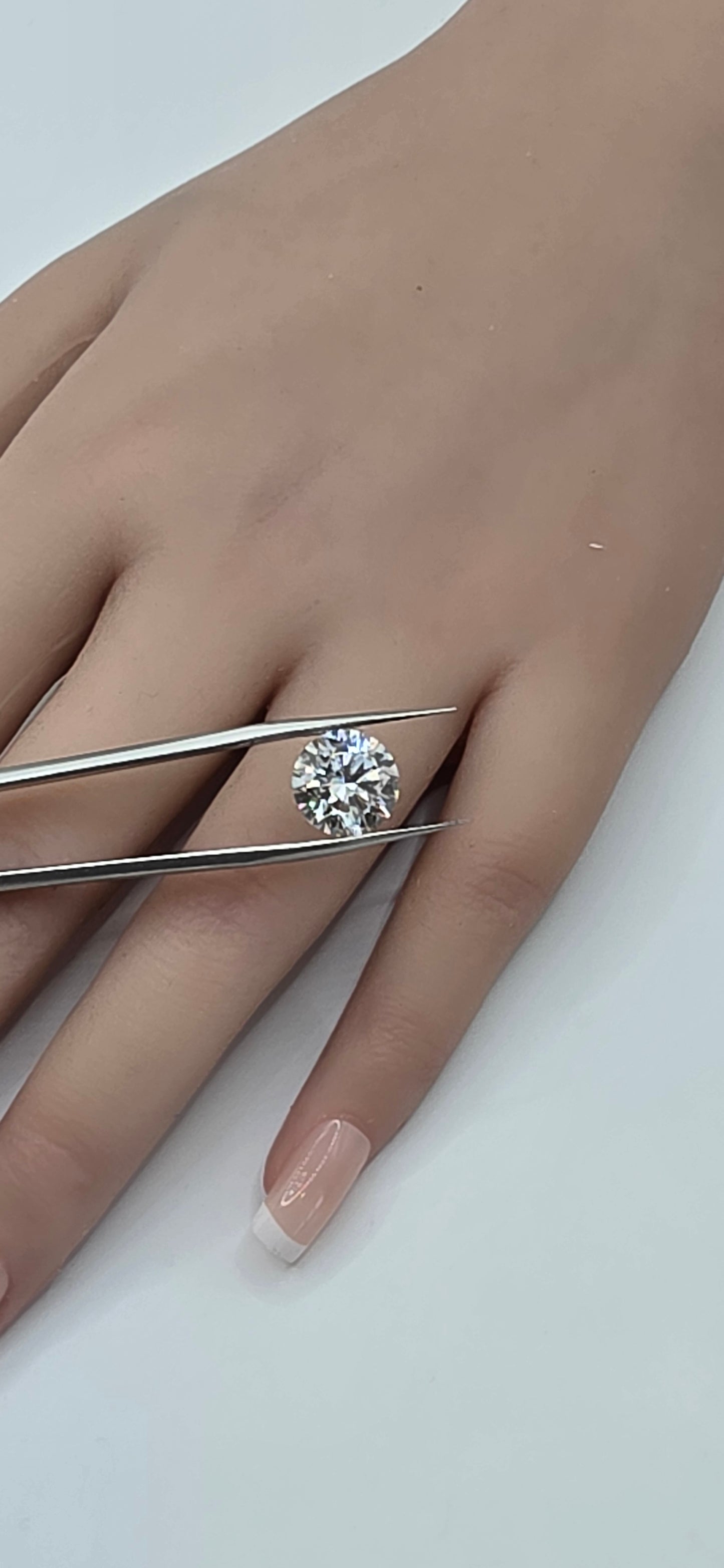 Diamond ring being held by tweezers on a hand with a white background