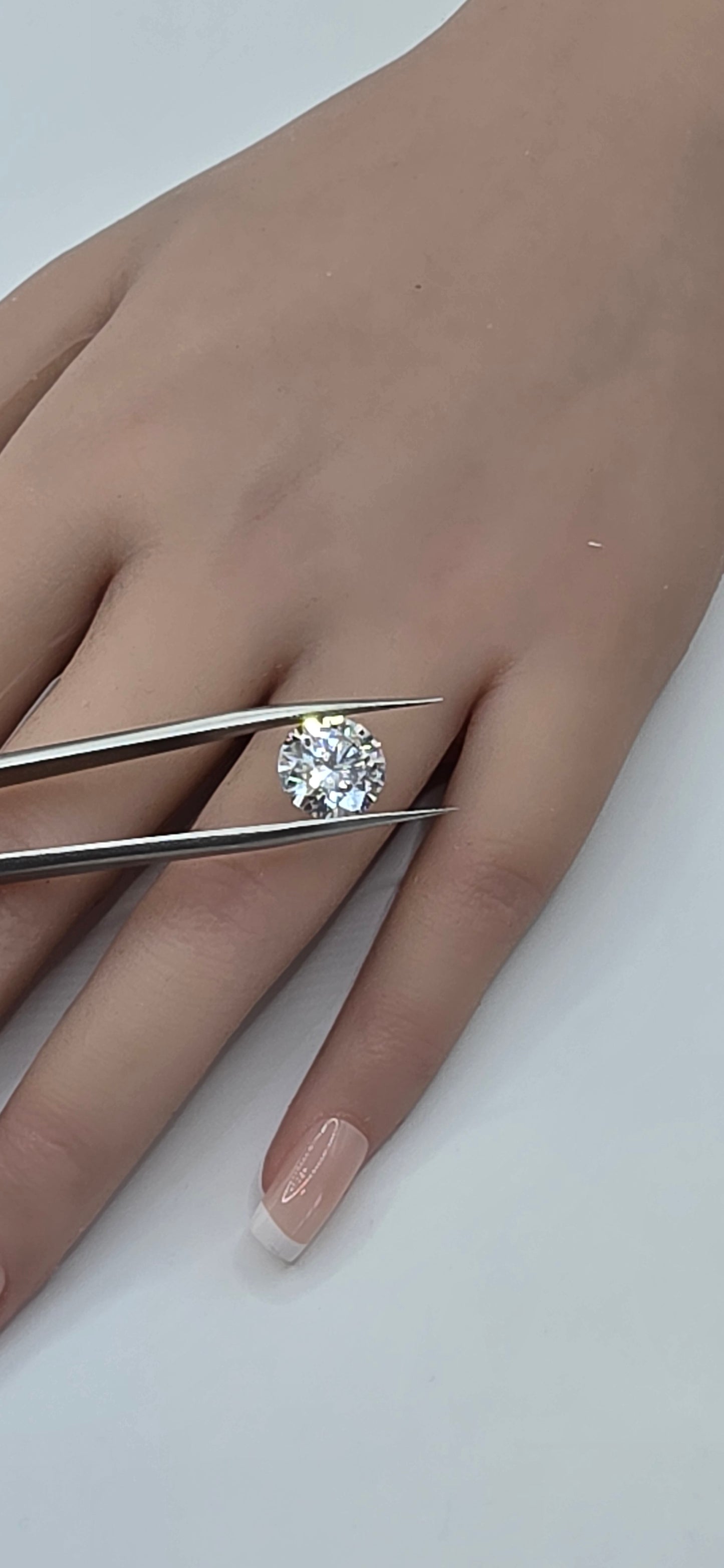 Diamond ring being held by tweezers on a hand with a white background