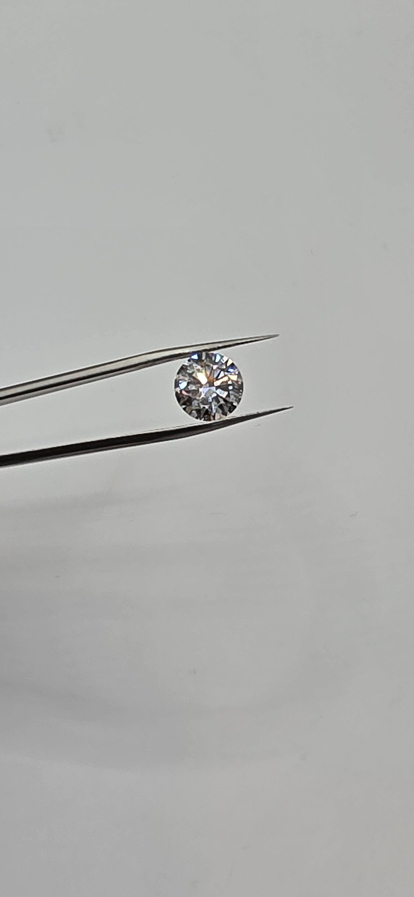 Diamond held between tweezers against a gray background