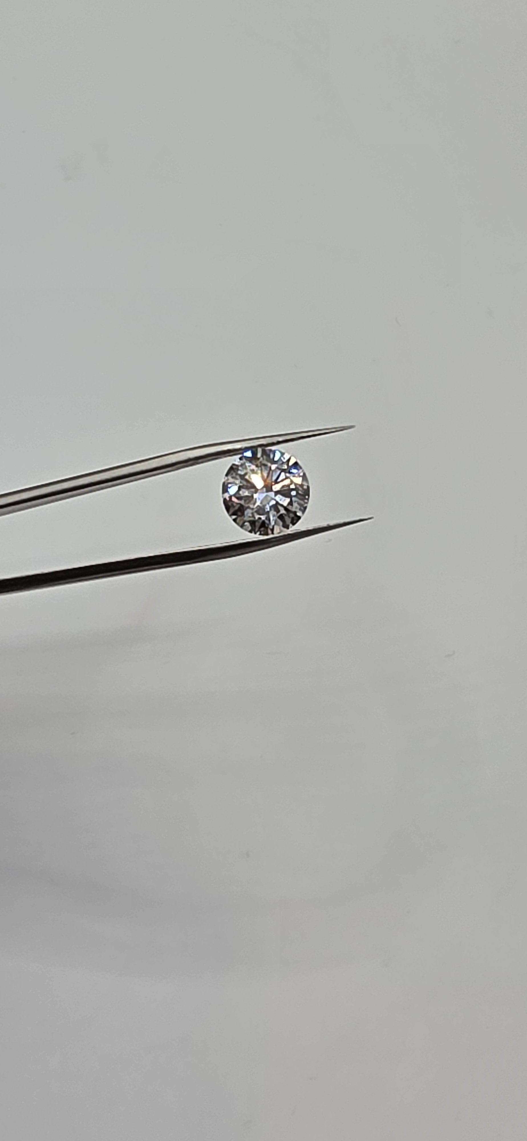 Diamond held between tweezers against a gray background