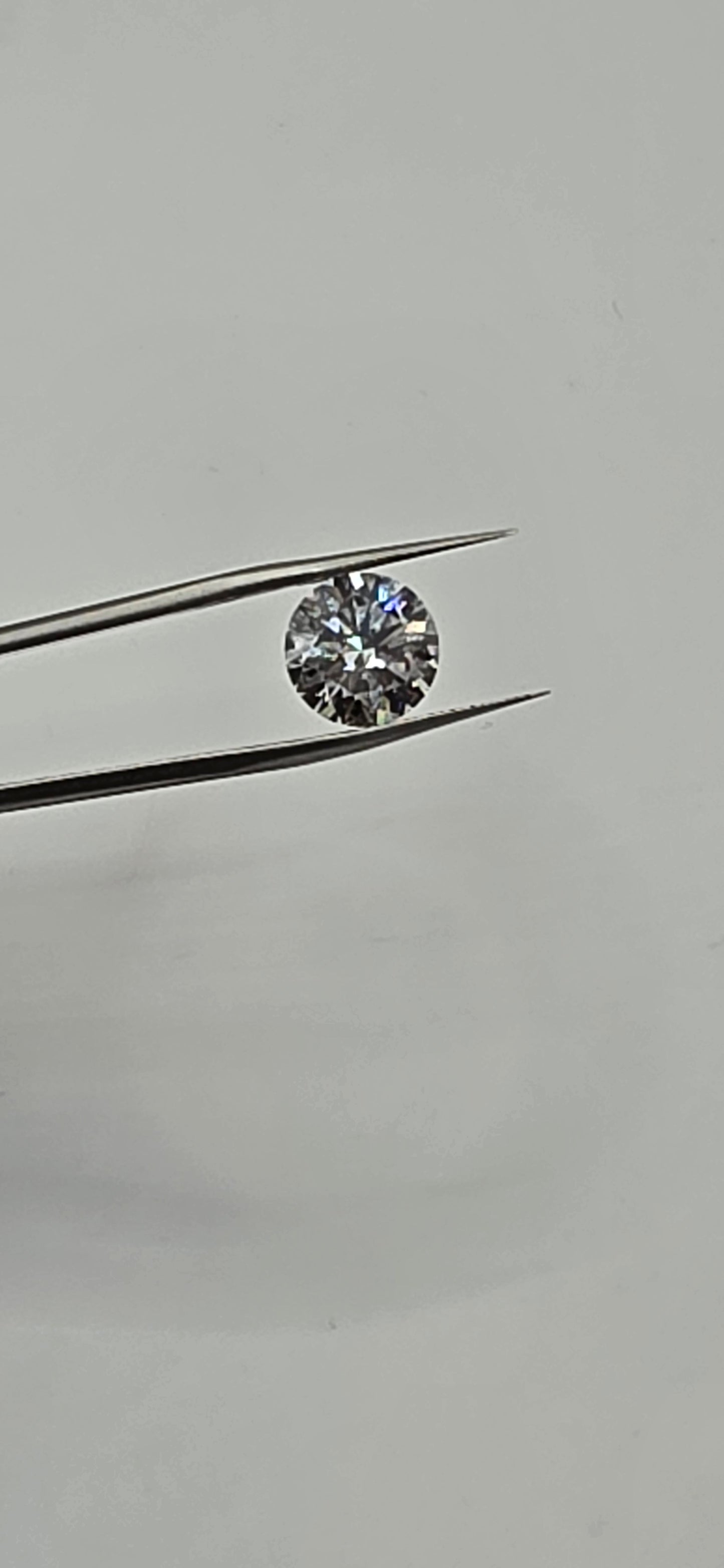 Diamond held between tweezers against a gray background
