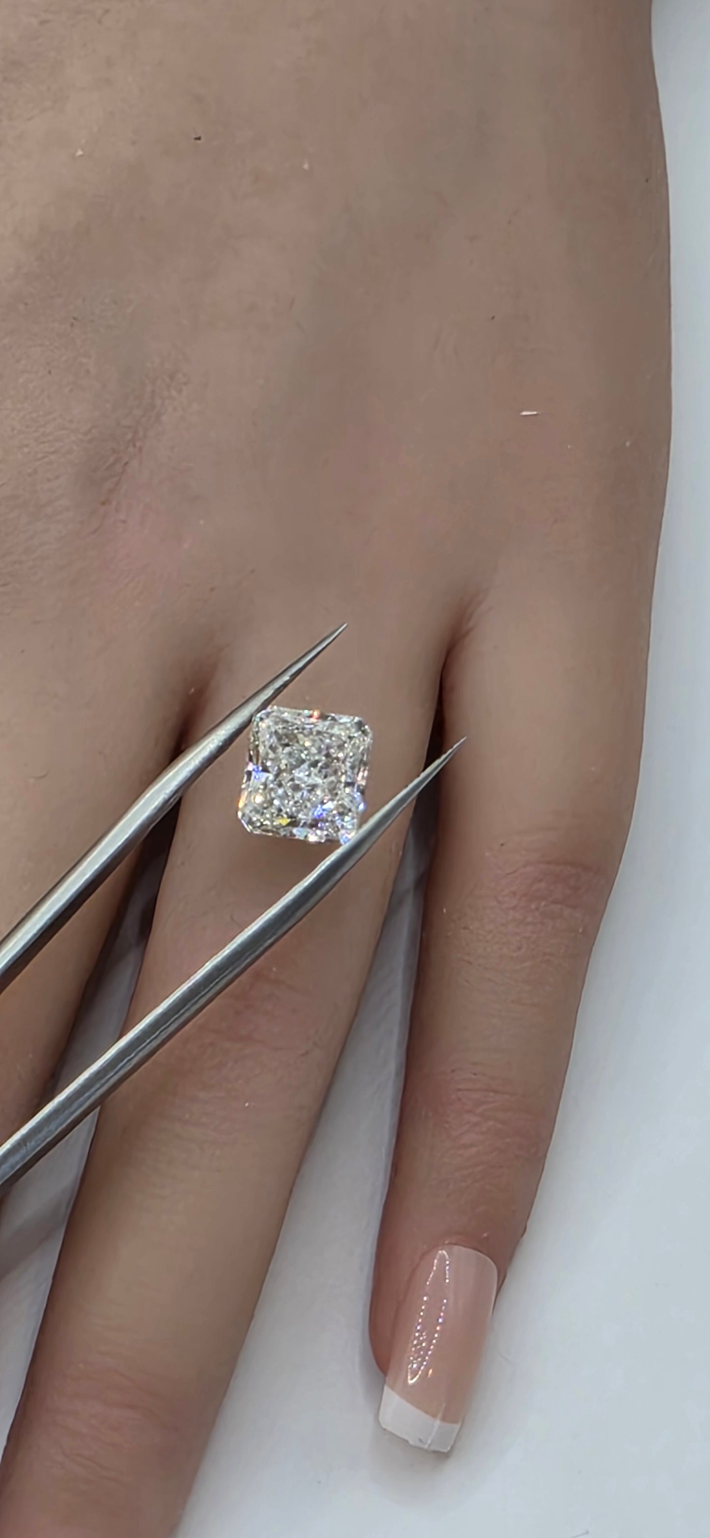 Diamond ring held by tweezers on a person's hand with a neutral background