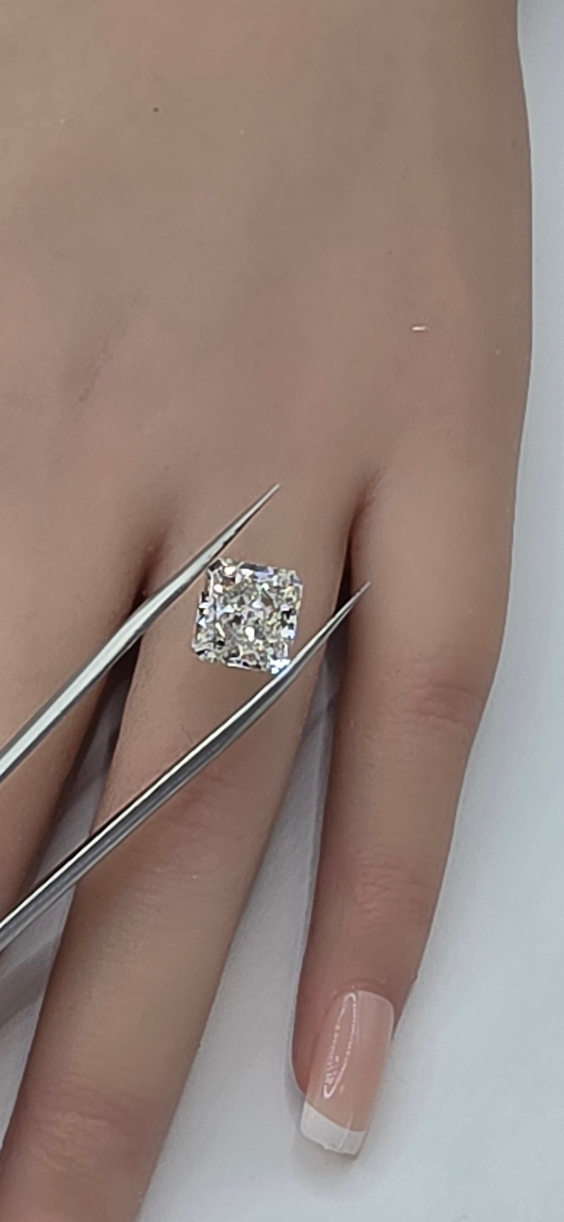 Diamond being held by tweezers against a person's finger on a white background