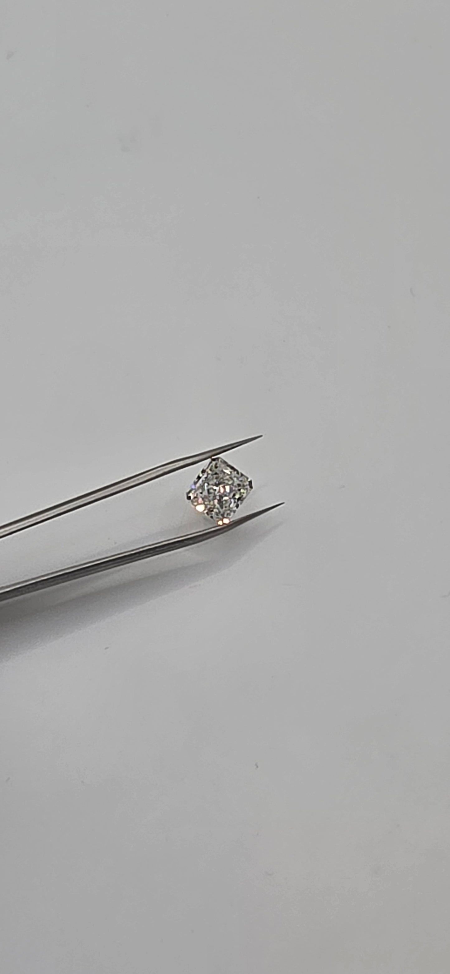 Diamond held between tweezers on a gray background