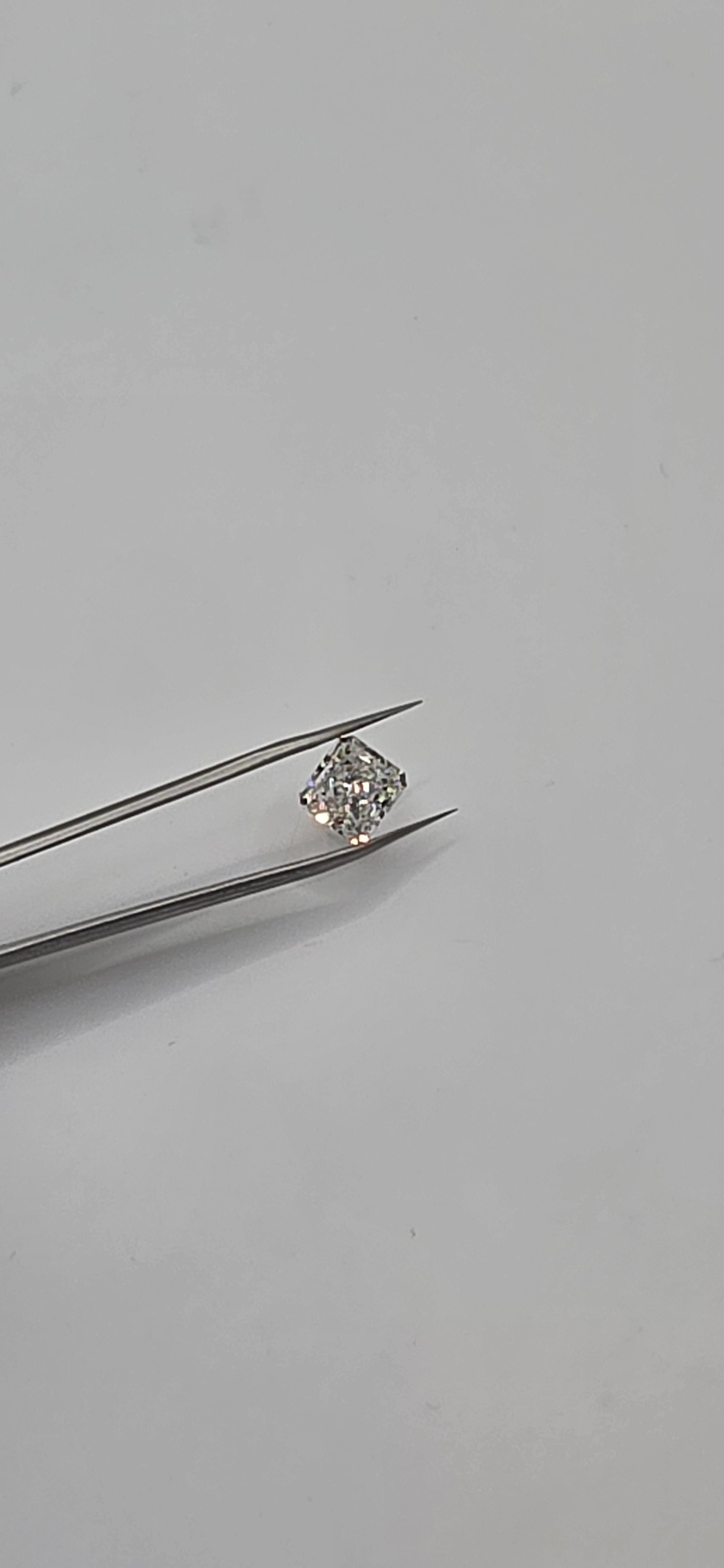 Diamond held between tweezers on a gray background