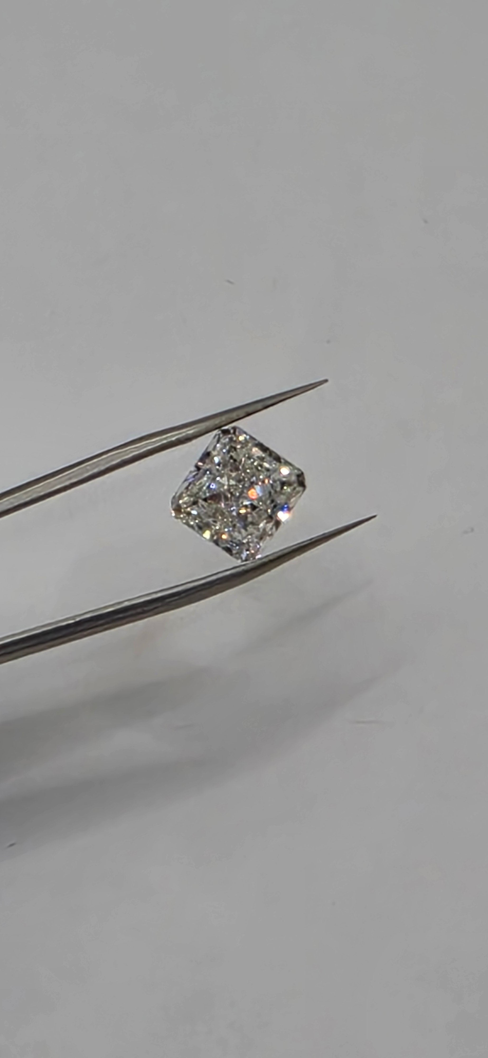 Diamond held between tweezers against a gray background