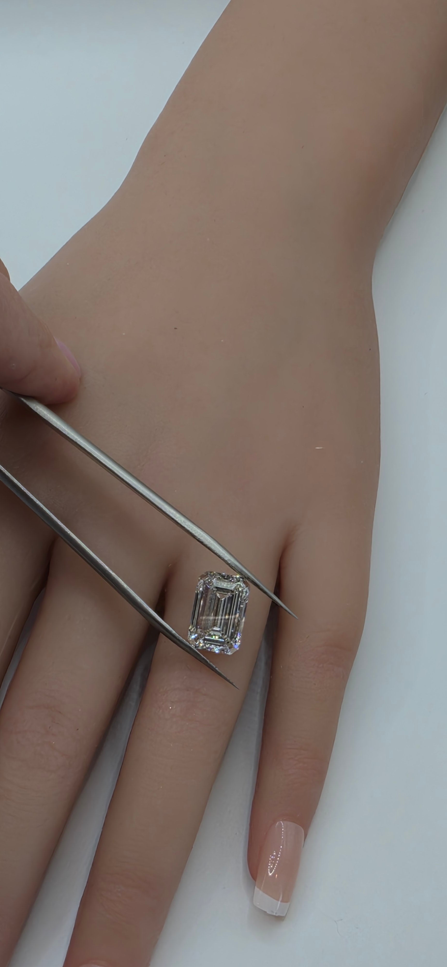 Close-up of a hand with a diamond ring being adjusted with tweezers on a white background