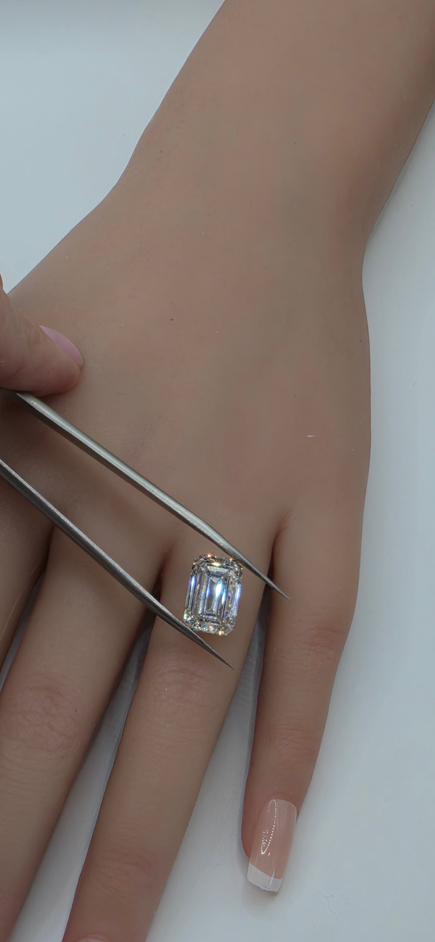 Close-up of a hand wearing a diamond ring with tweezers adjusting it on a white background