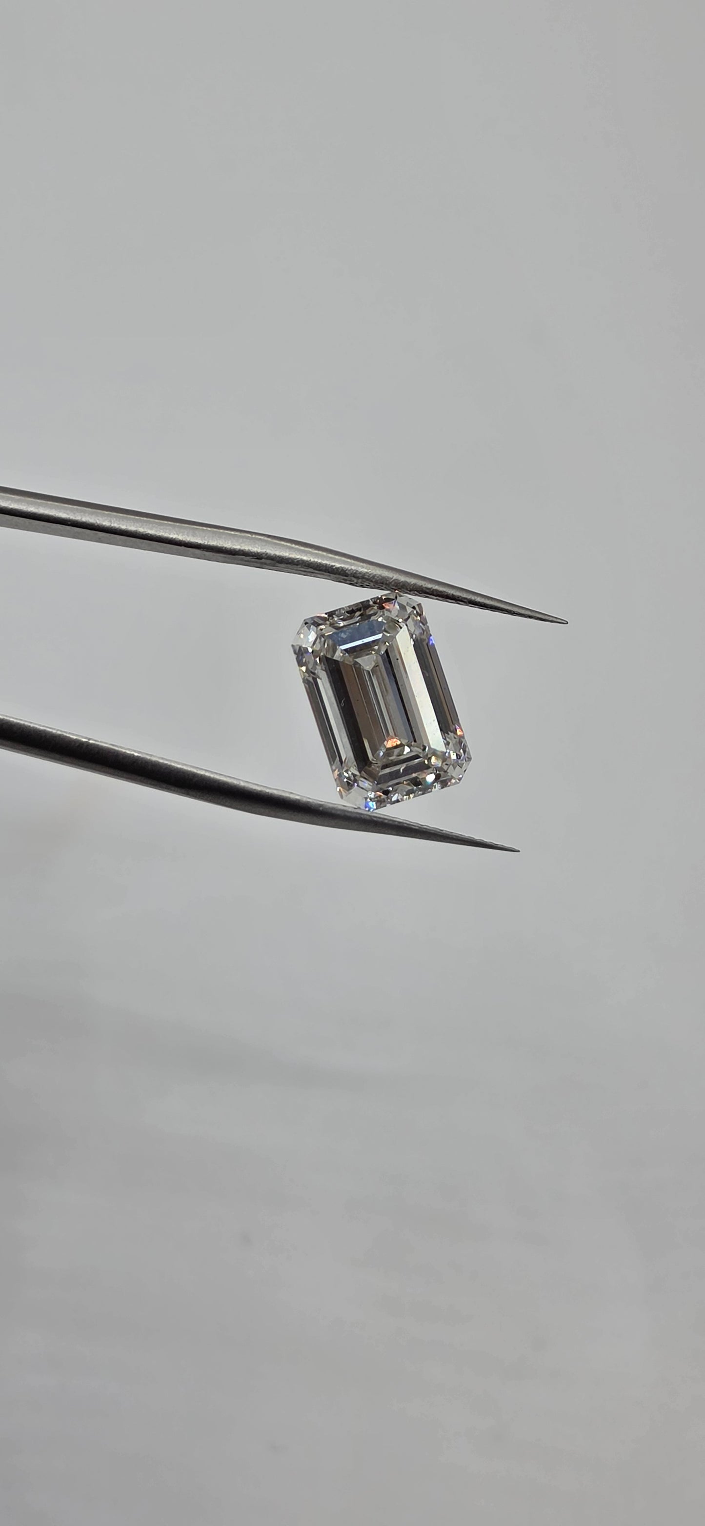 Diamond held between tweezers against a gray background