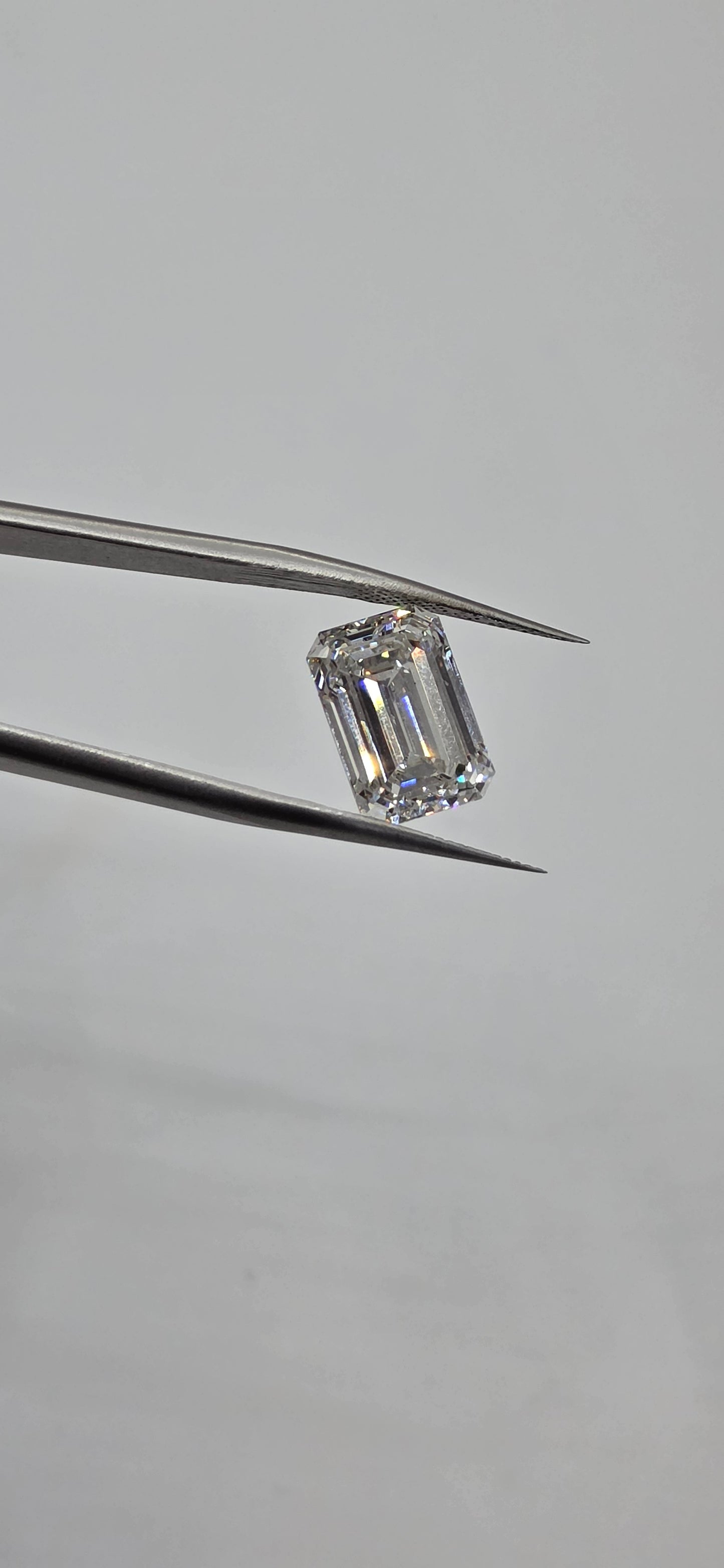 Diamond held between tweezers on a gray background