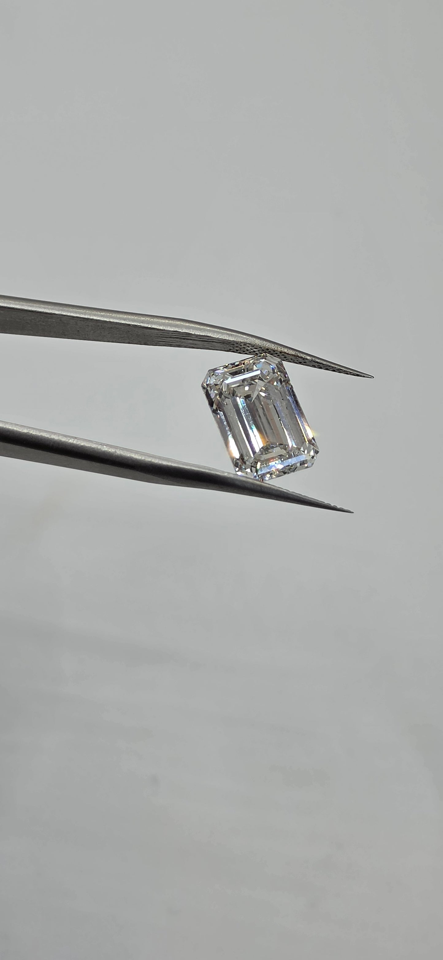 Diamond held between tweezers on a gray background