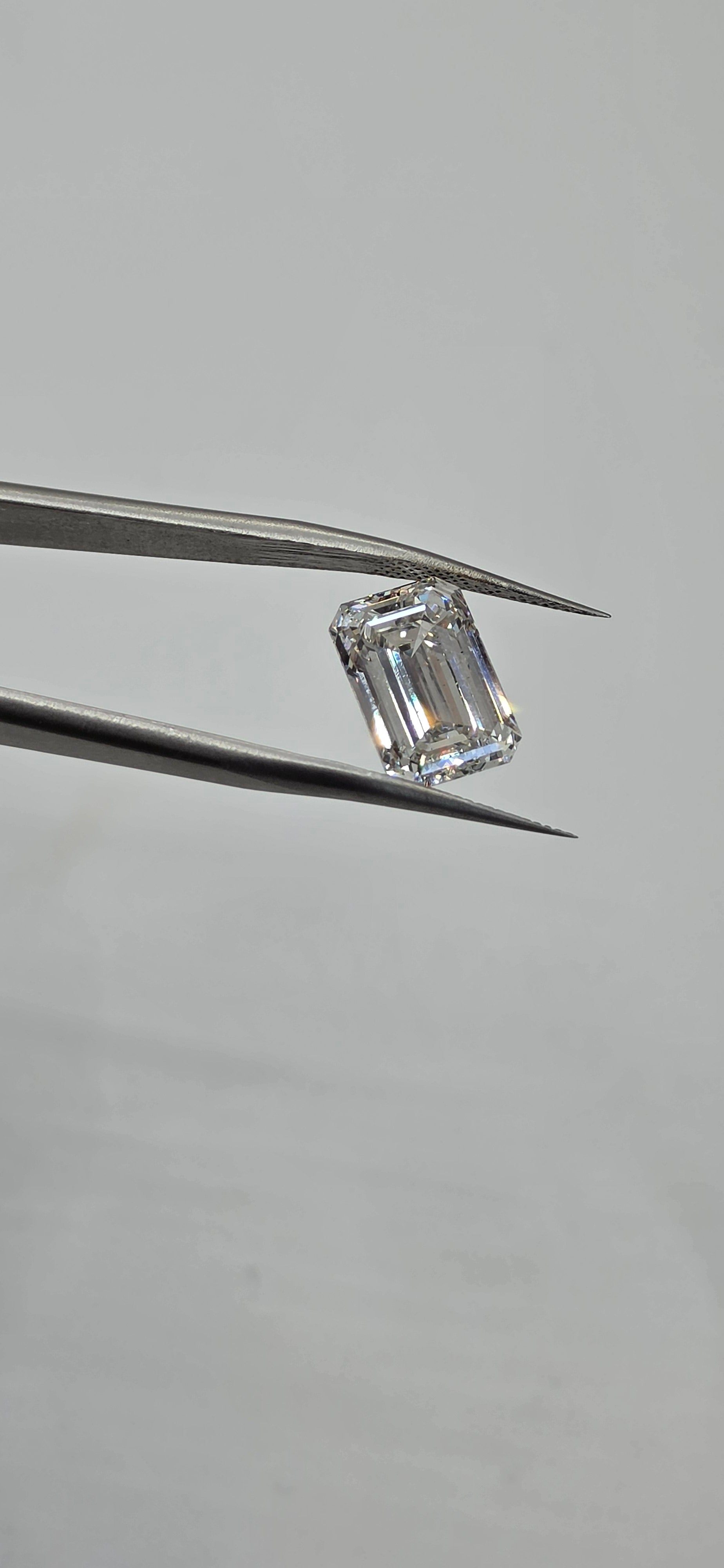 Diamond held between tweezers on a gray background