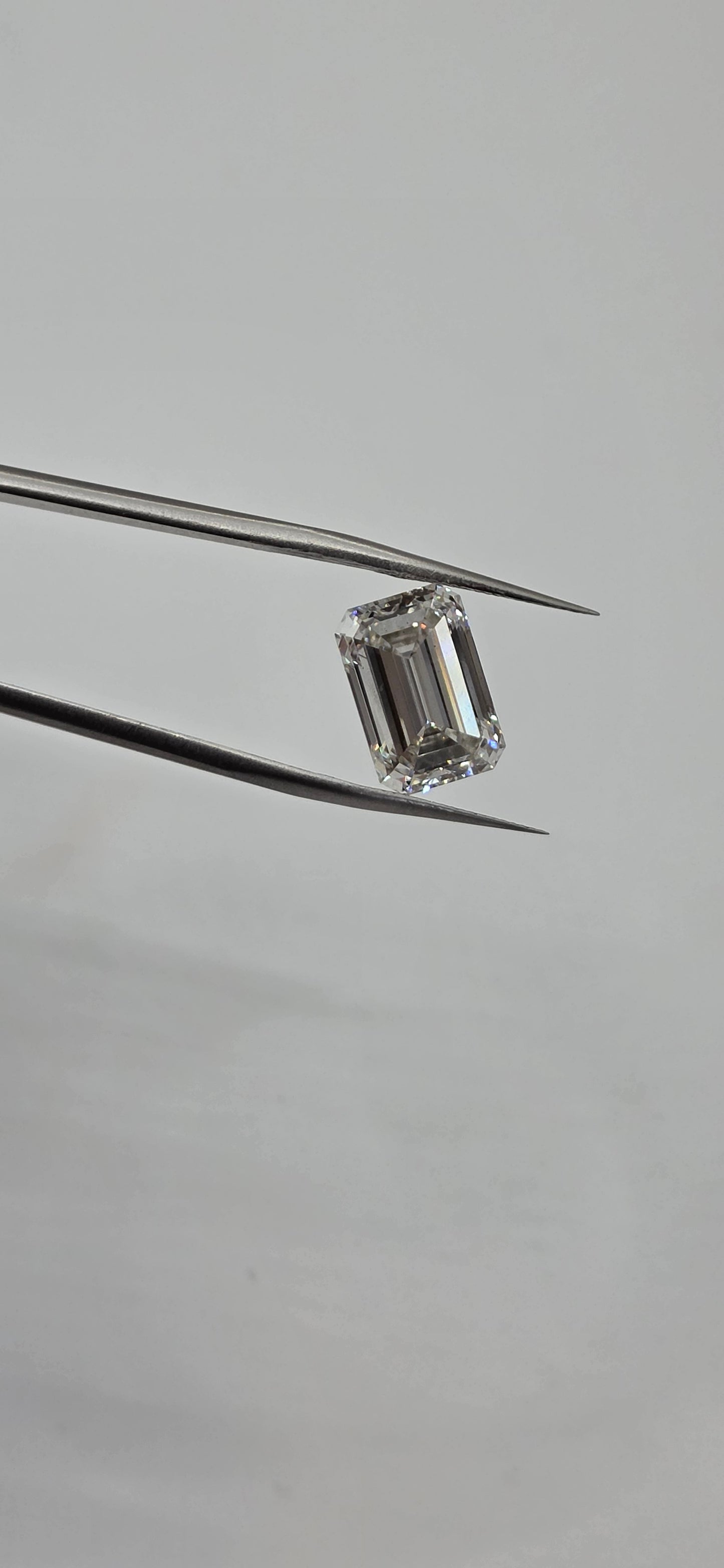 Diamond held between tweezers on a gray background