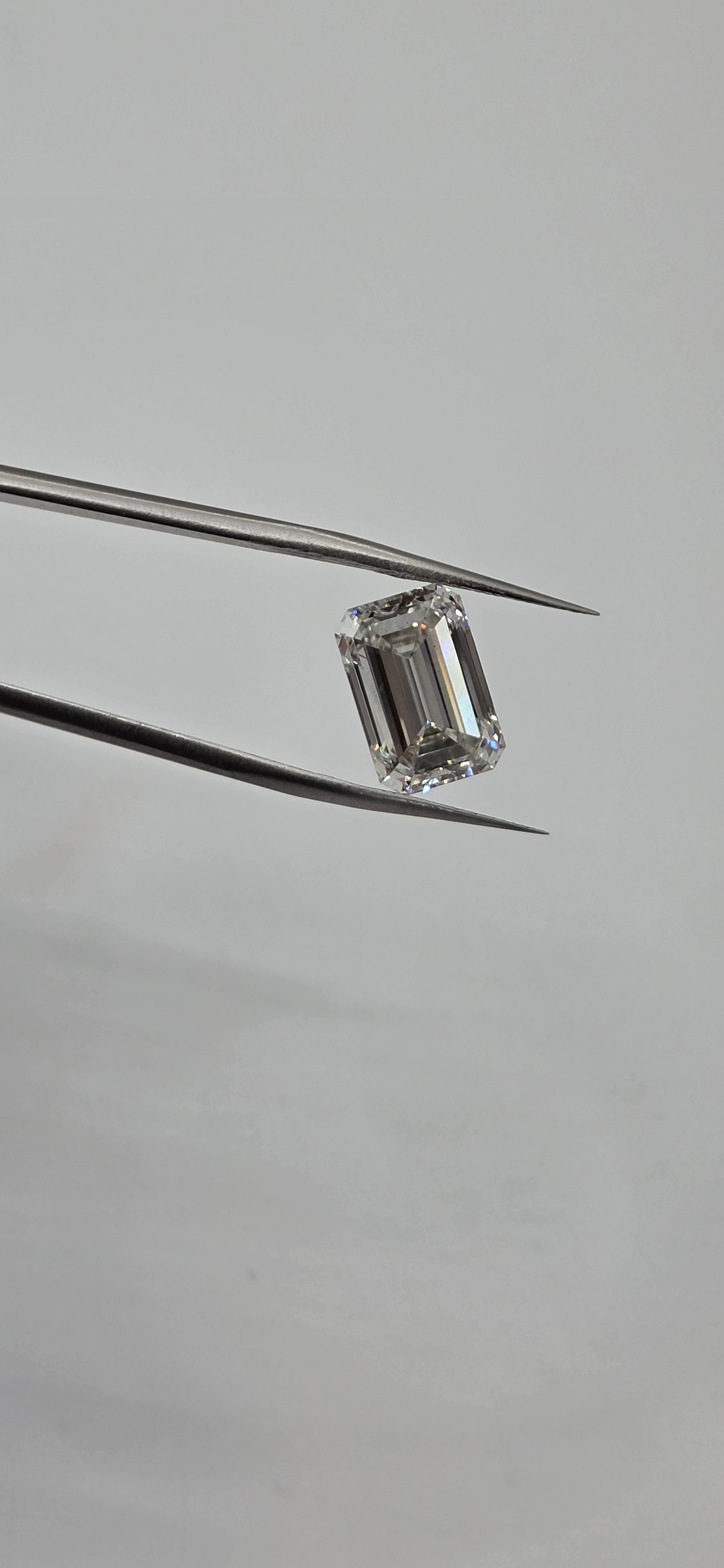 Diamond held between tweezers on a gray background