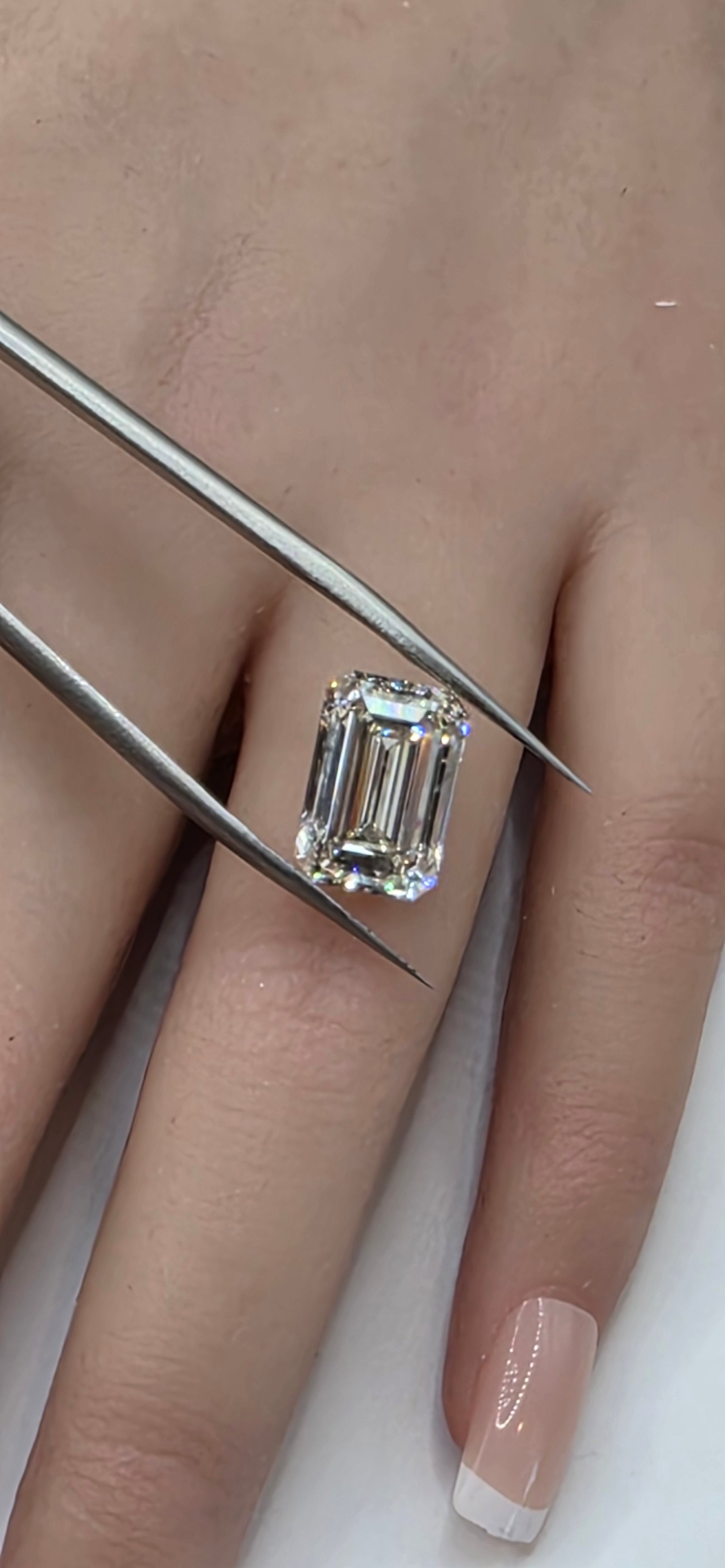 Diamond ring on a finger with tweezers adjusting it, against a neutral background