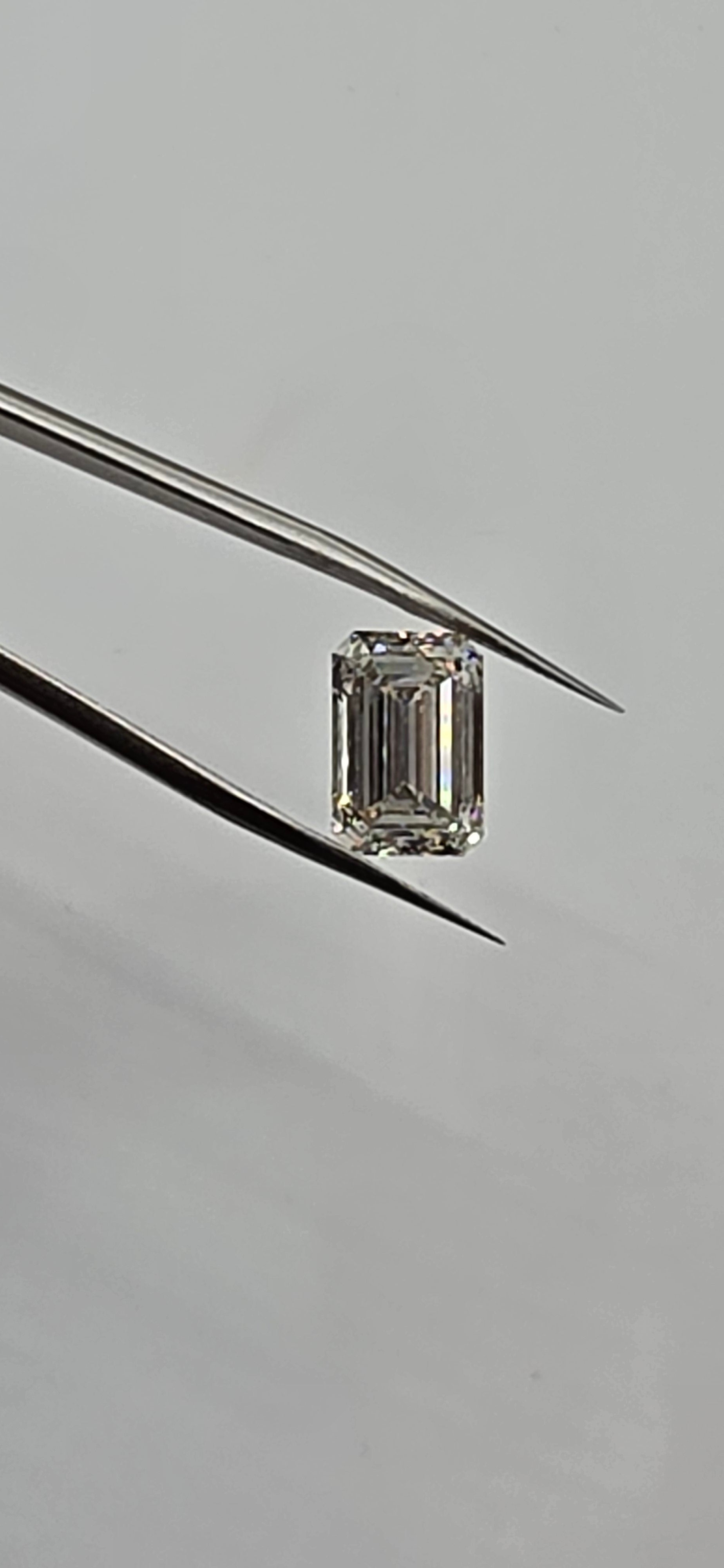 Emerald-cut diamond held between tweezers on a gray background