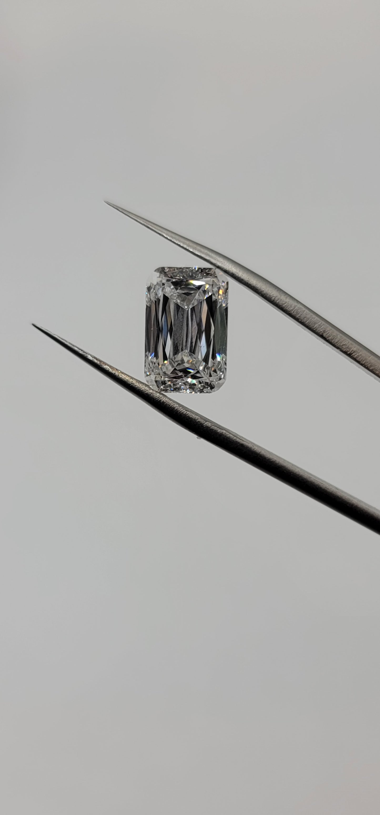 Diamond held between tweezers on a gray background
