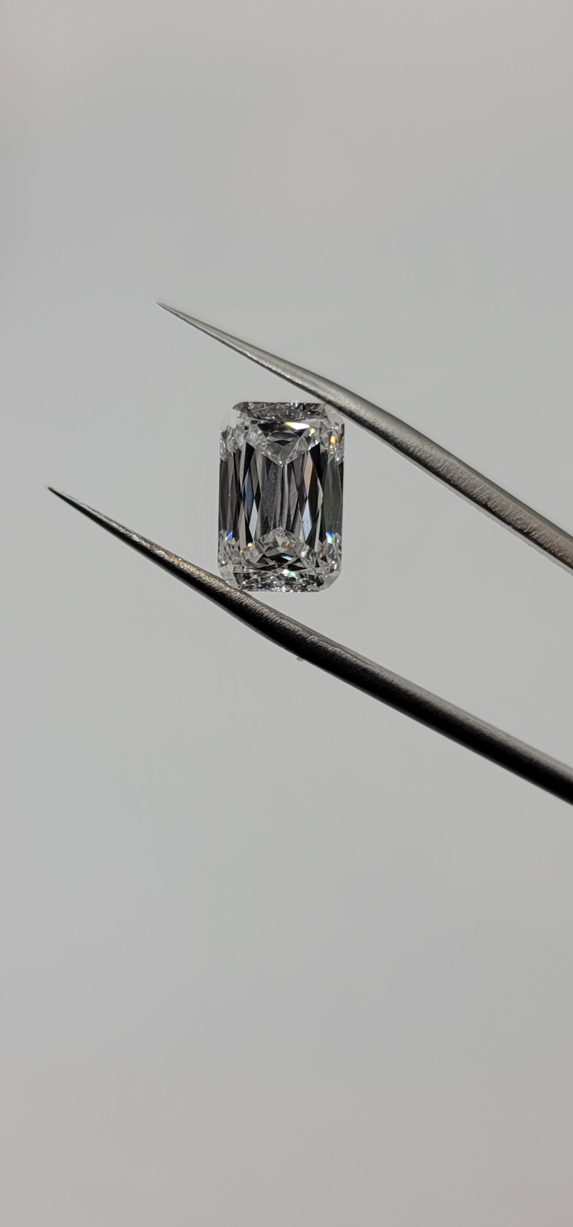 Diamond held between tweezers on a gray background