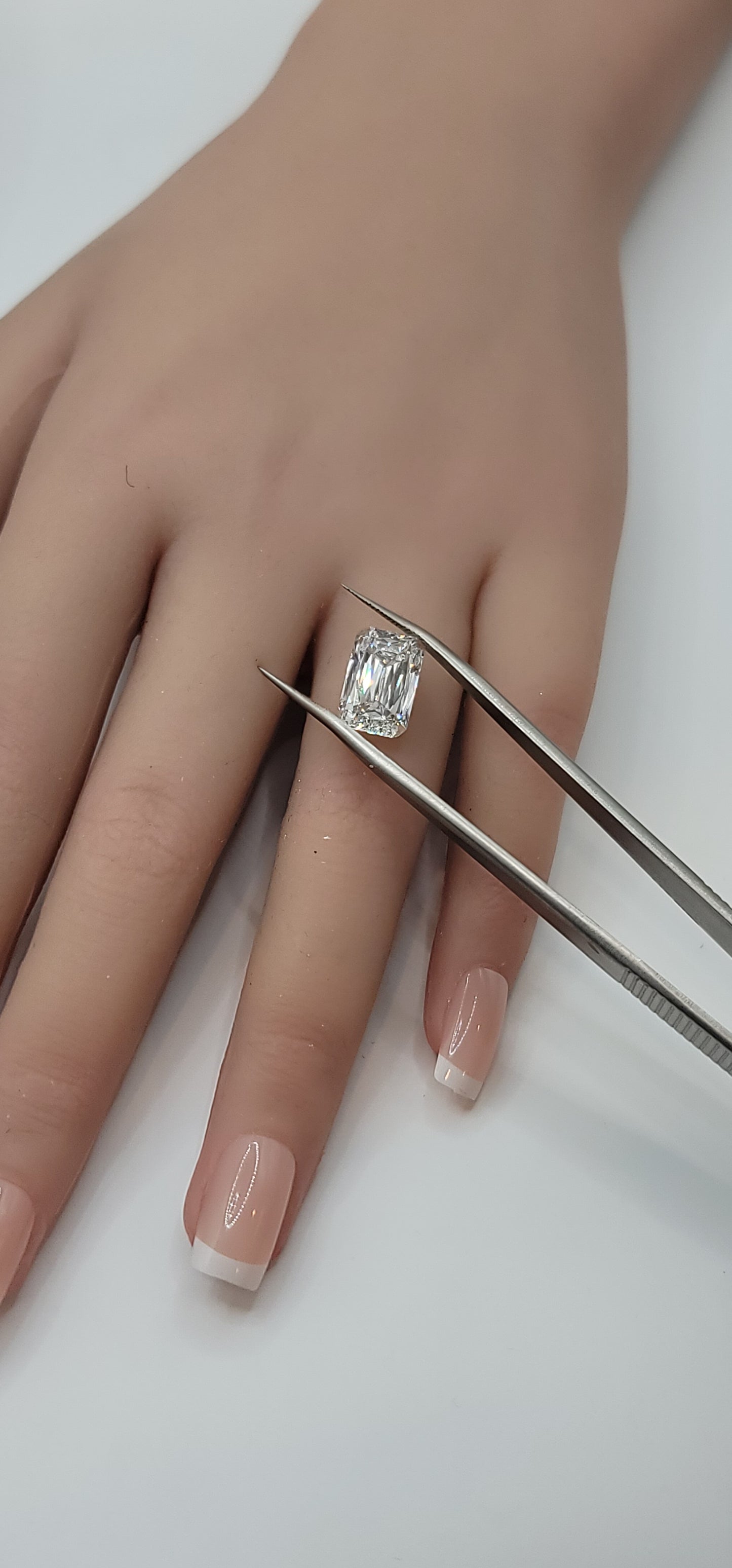 Diamond ring on a hand with tweezers against a white background