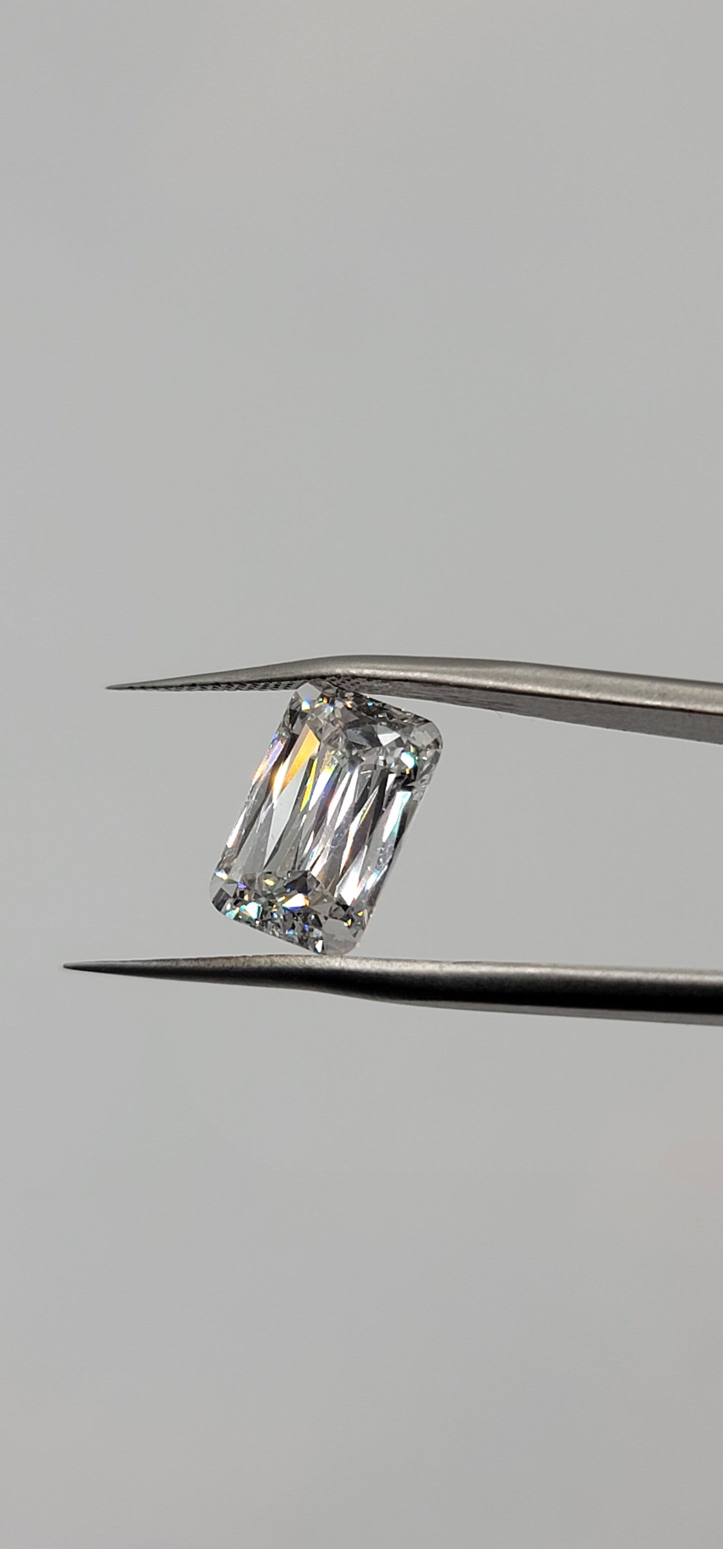 Diamond held between tweezers on a gray background