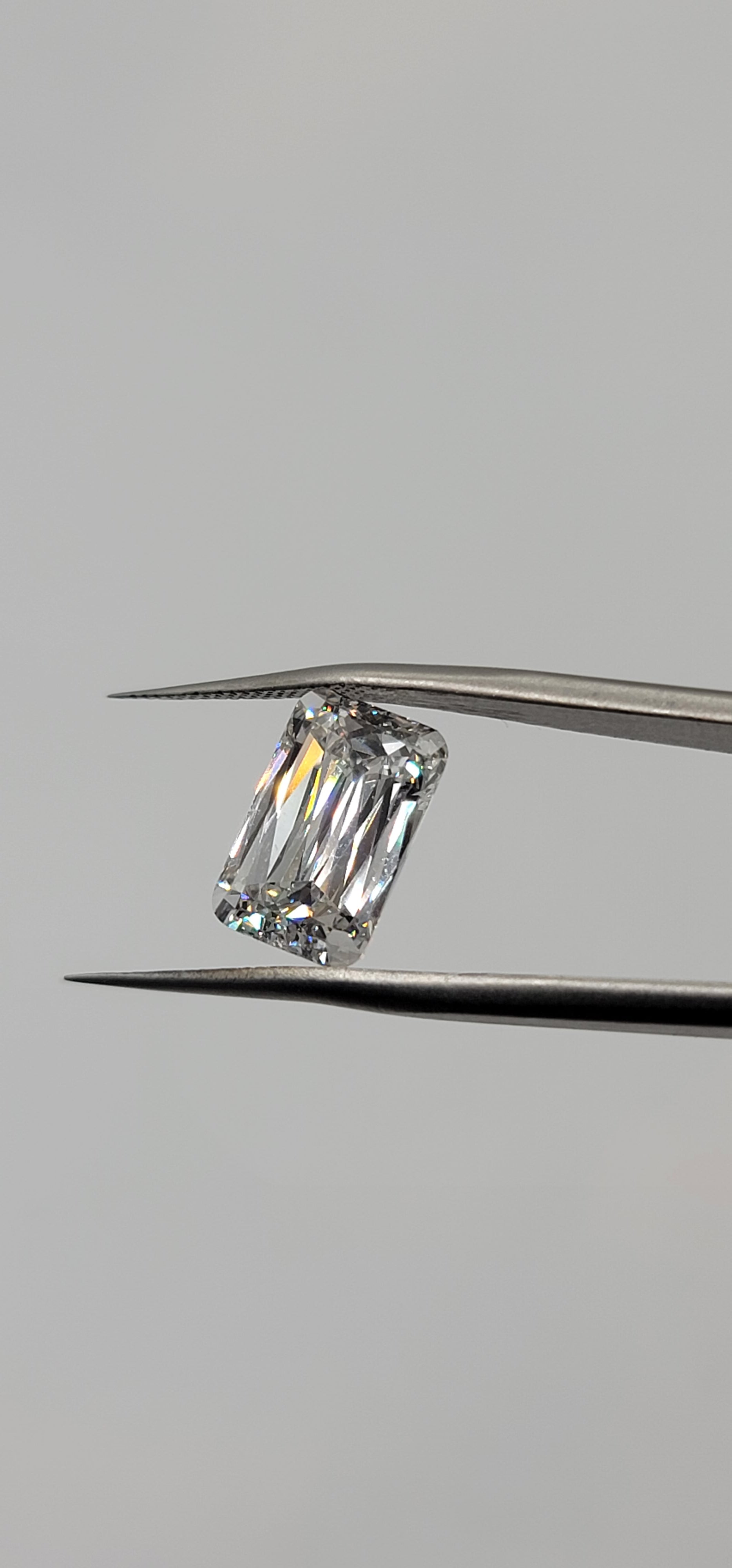 Diamond held between tweezers on a gray background