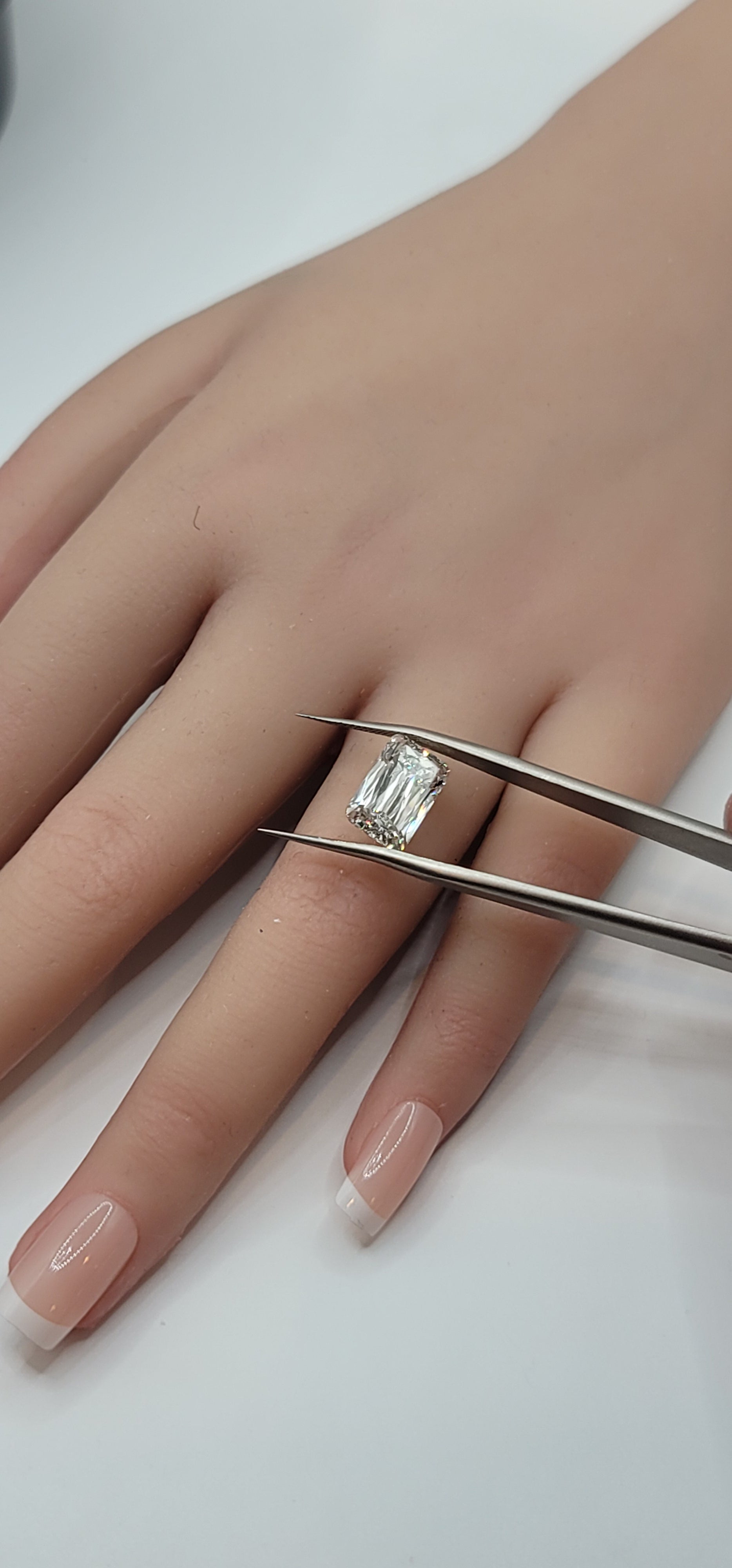 Hand with a diamond ring being adjusted with tweezers on a white background
