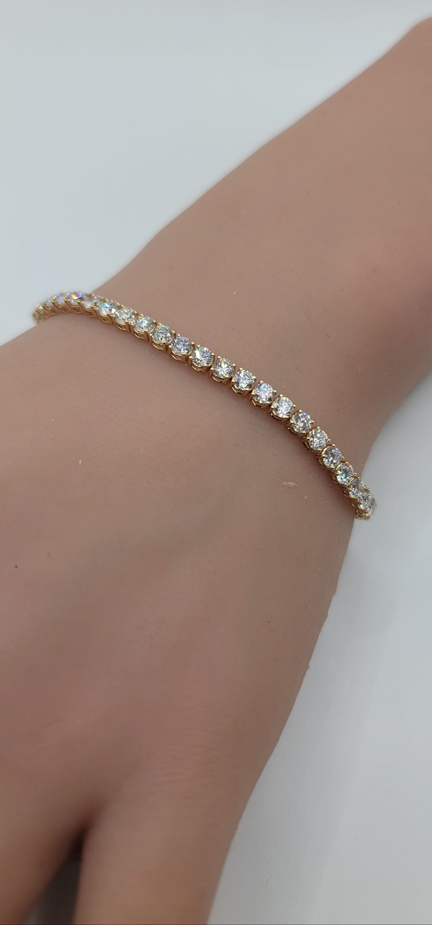 Yellow gold bracelet with clear stones on a wrist against a white background