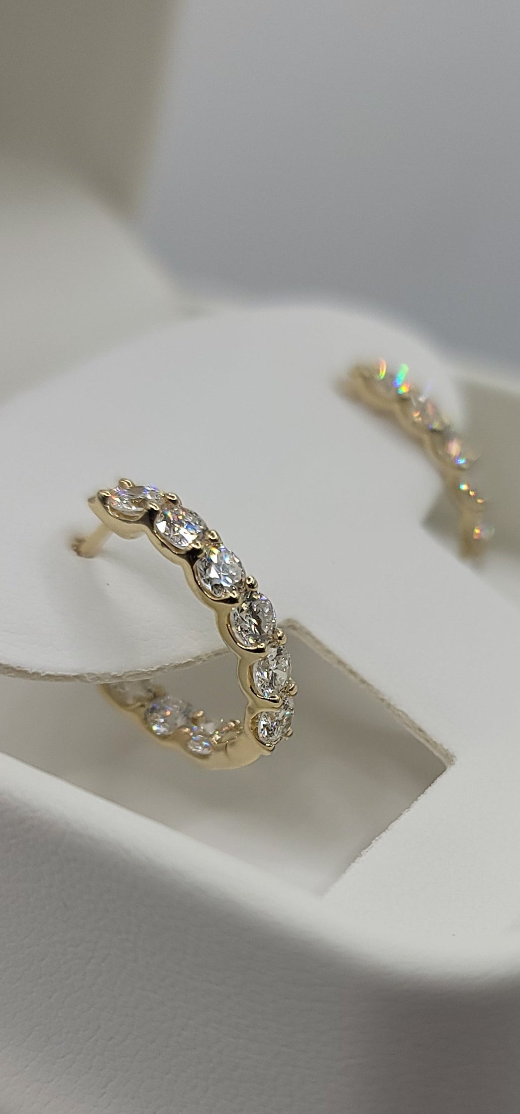 Gold hoop earrings with gemstones on a white stand
