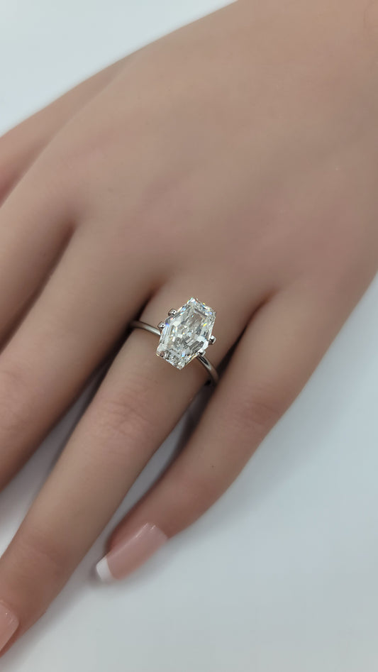 A close-up of a hand wearing a silver ring with a large hexagonal cut lab diamond, set against a plain light background.