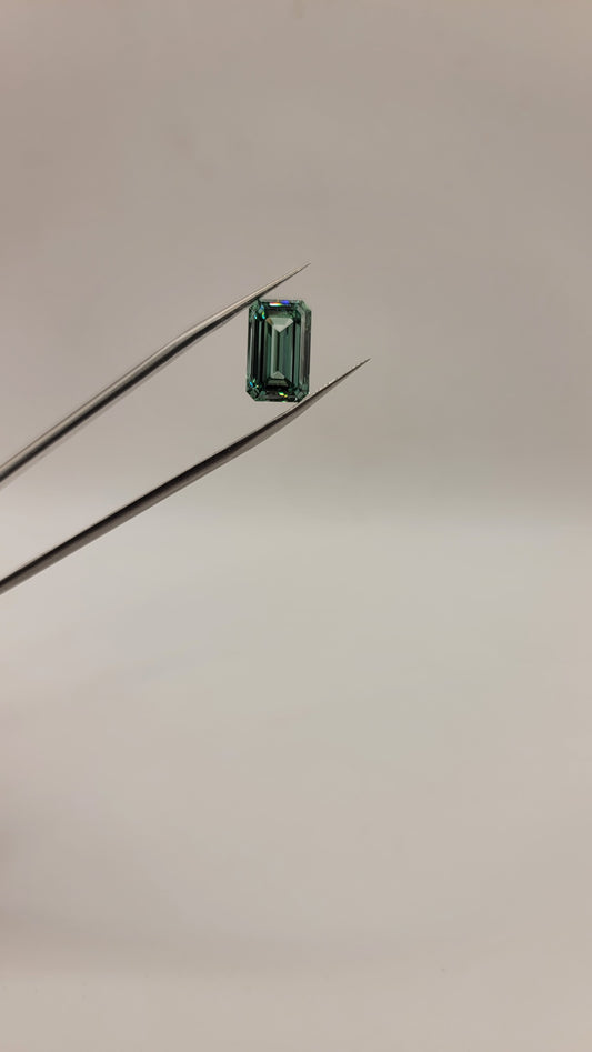 A small rectangular emerald-cut green diamond held between two metal tweezers against a plain light background.