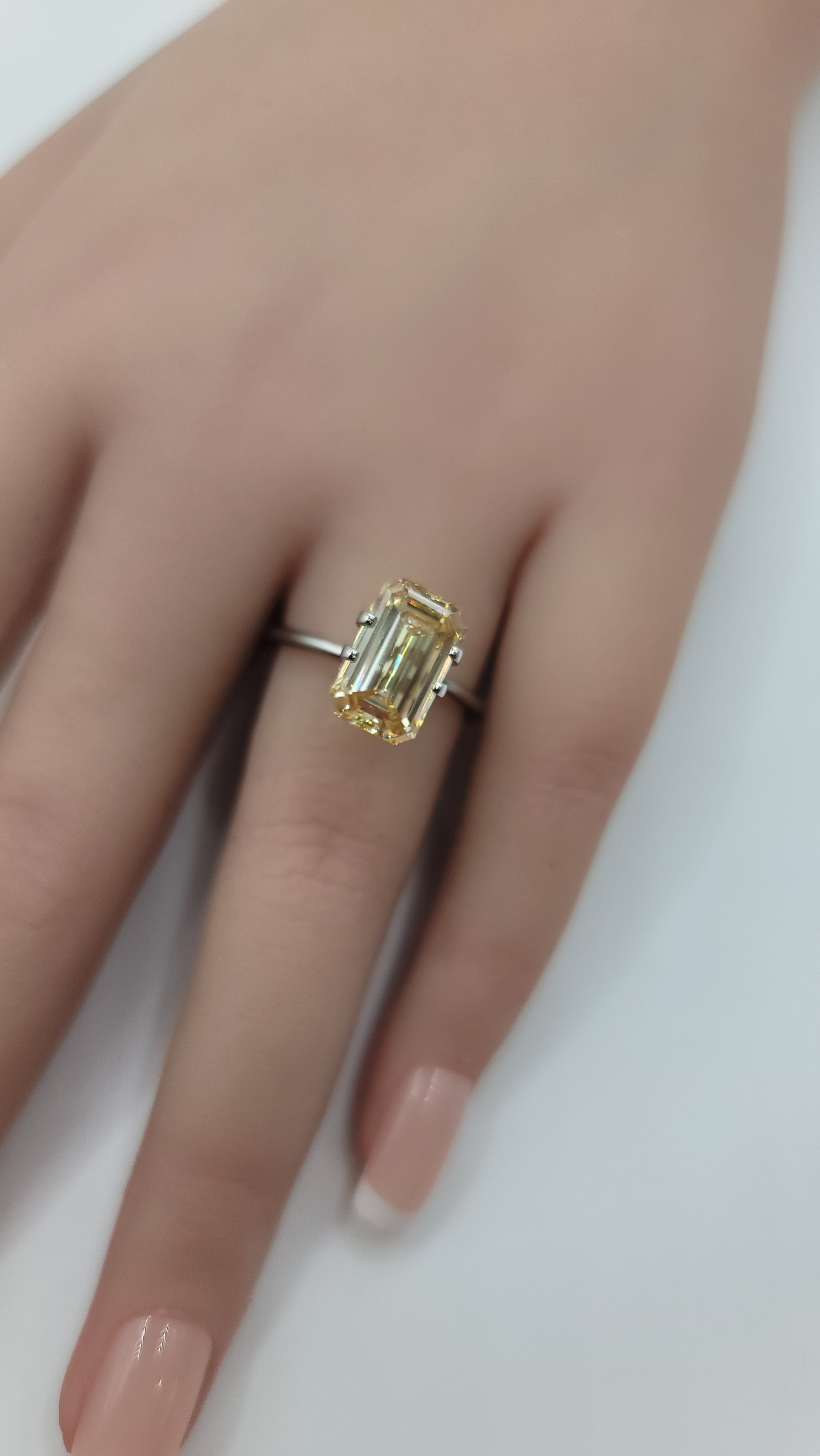  yellow emerald-cut lab grown diamond with a gold band on a plain light background.