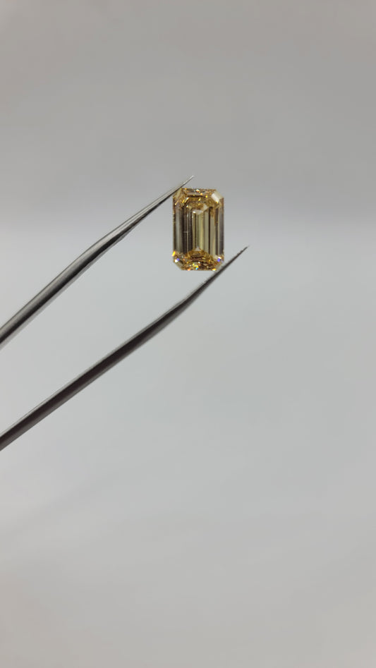 Yellow Lab Grown diamond held between metal tweezers against a plain light gray background.