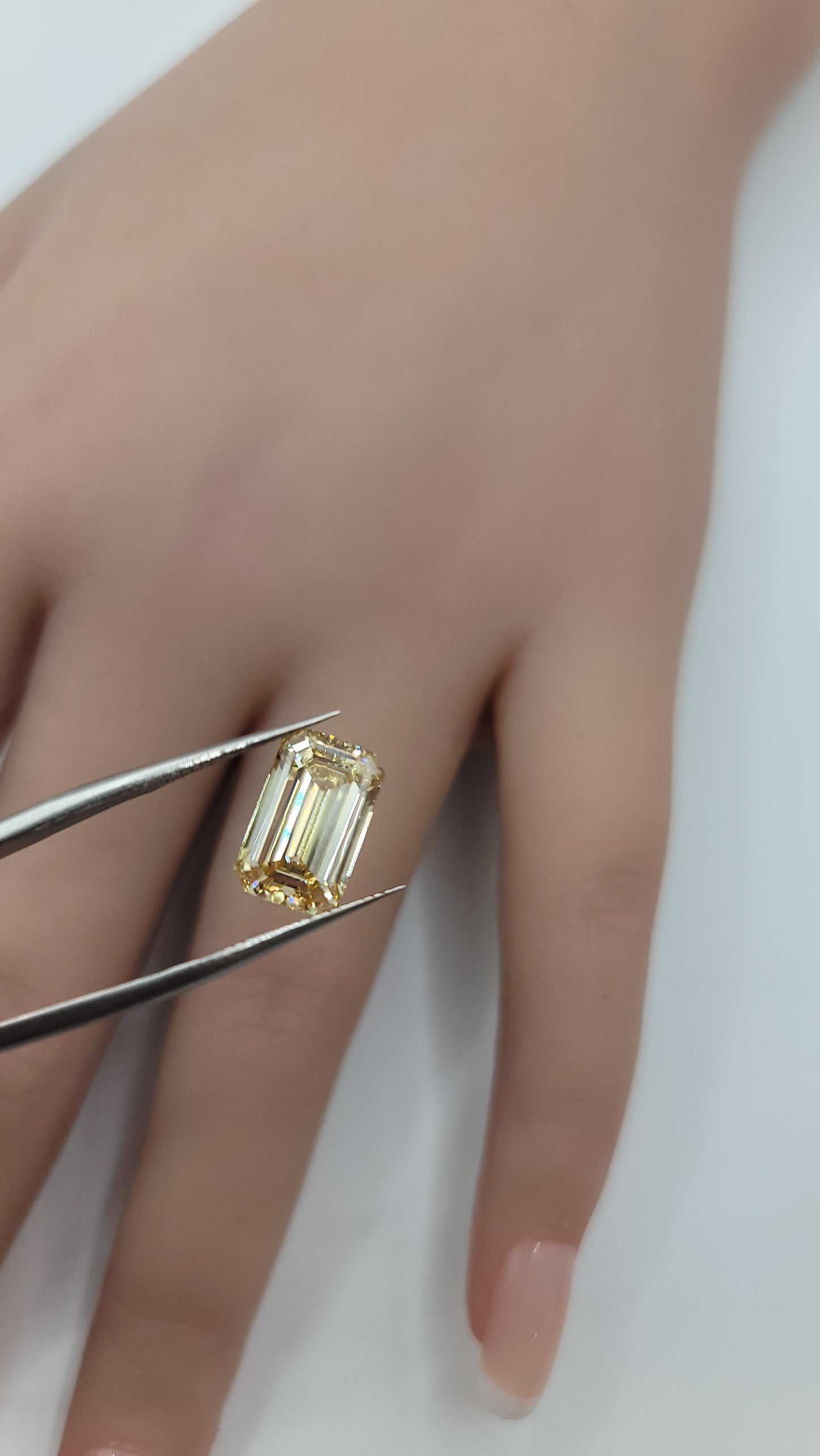 Yellow lab grown diamond held in tweezers over a hand