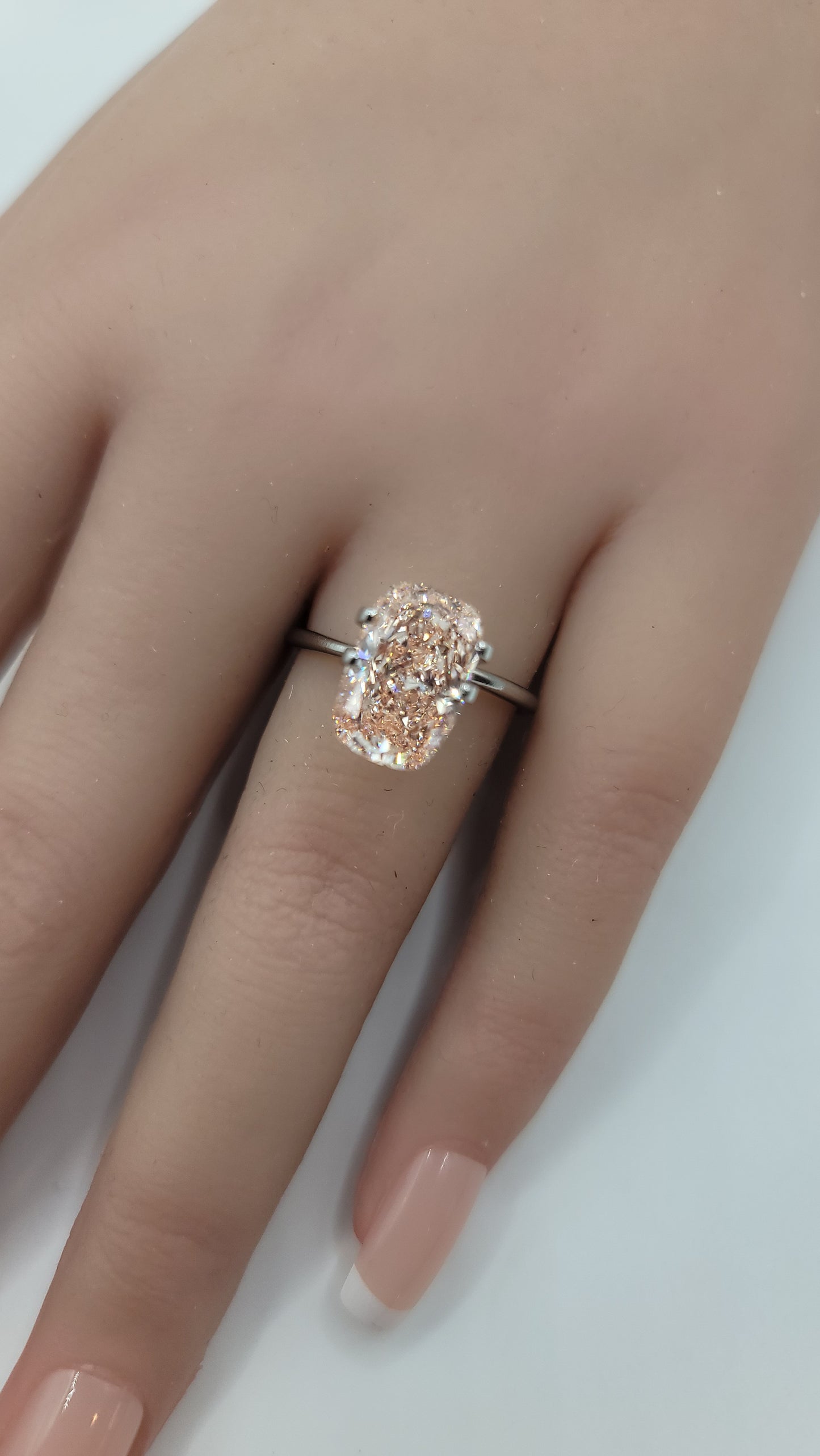 A close-up of a hand wearing a ring with a large cushion-cut lab grown pink diamond  in a silver-toned setting.