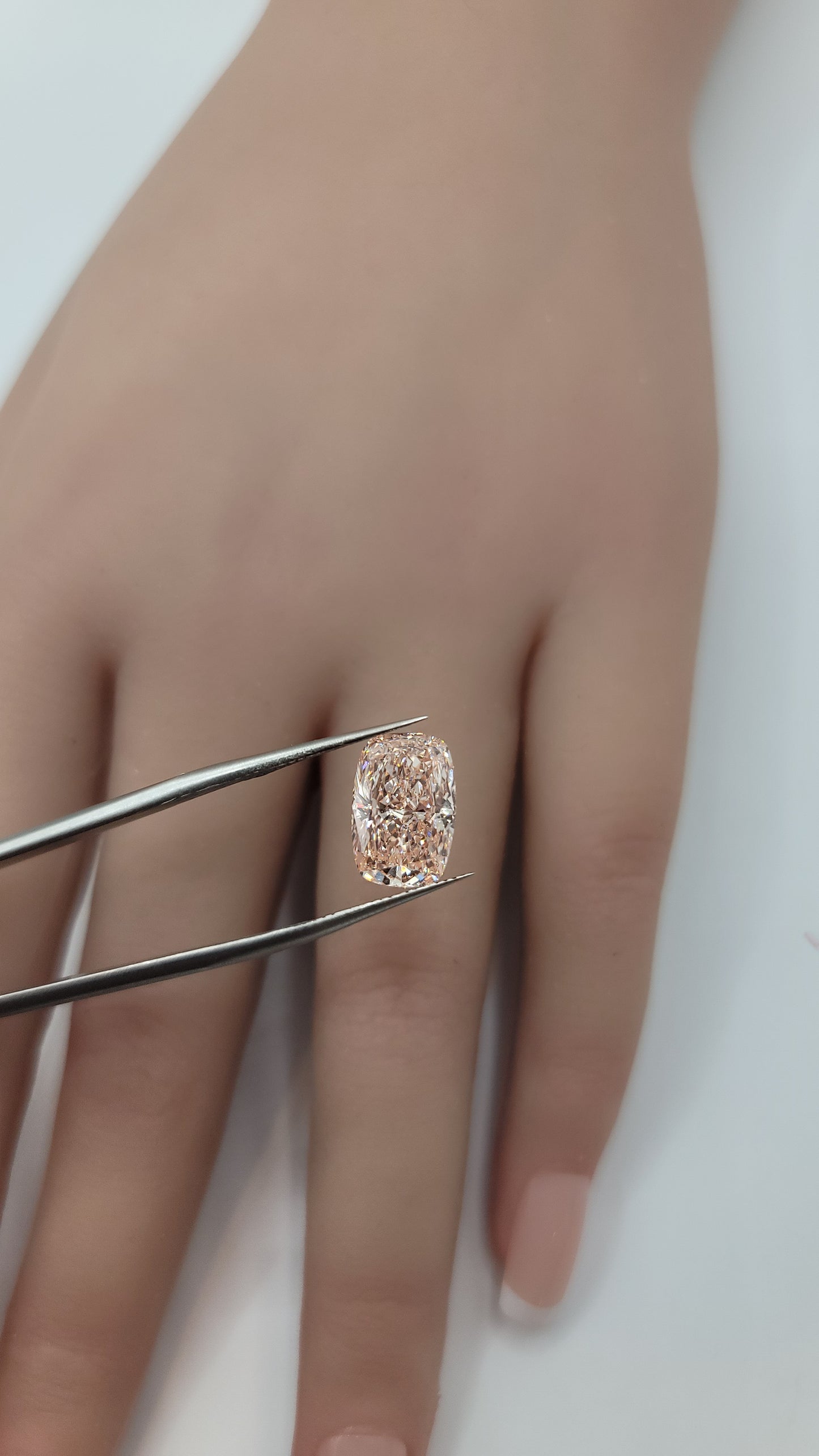 A close-up of a hand holding a pink lab grown diamond between metal tweezers against a plain light background