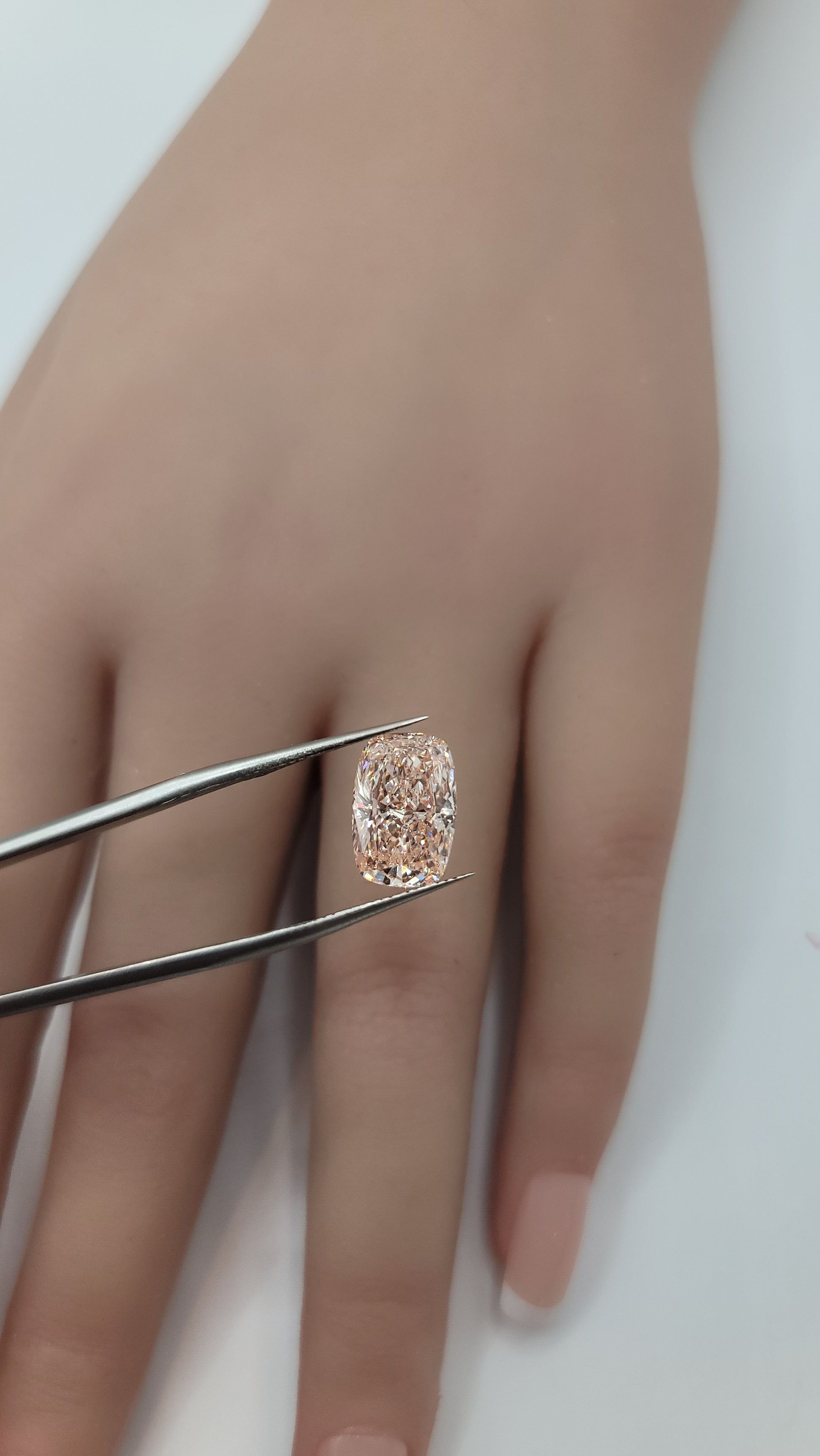 A close-up of a hand holding a pink lab grown diamond between metal tweezers against a plain light background