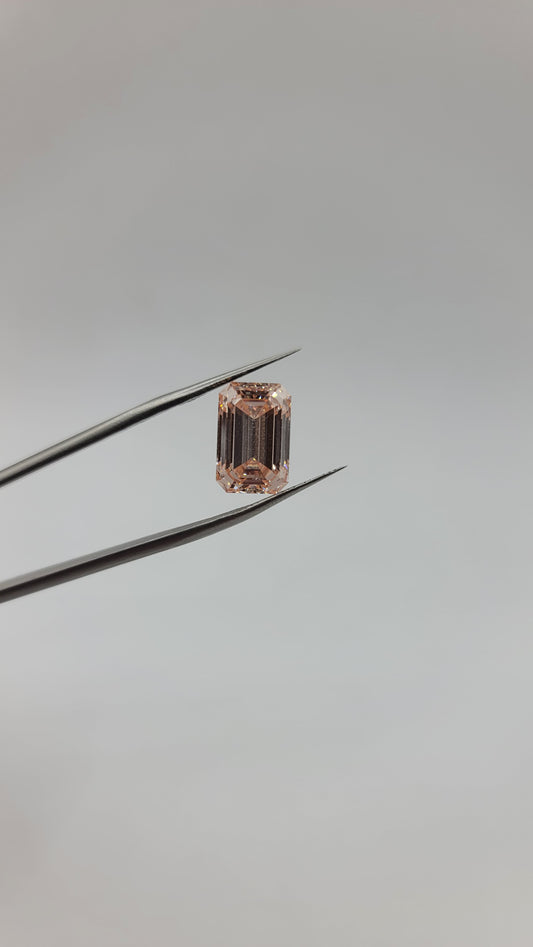 A rectangular emerald-cut pink lab diamond held between two metal tweezers against a plain light gray background.