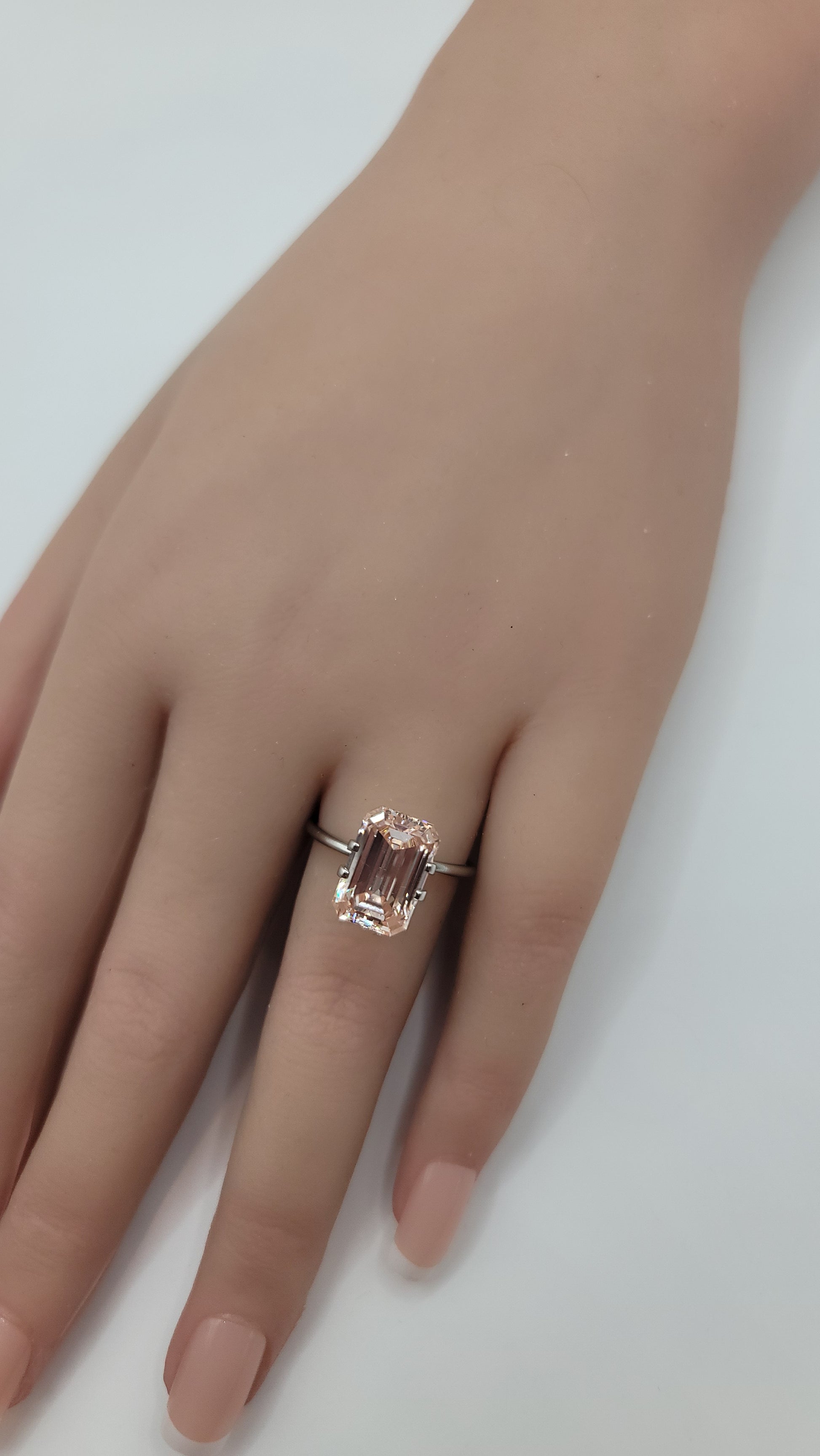 A silver-toned ring featuring an emerald-cut pink lab diamond, shown worn on a person's ring finger against a plain white background.