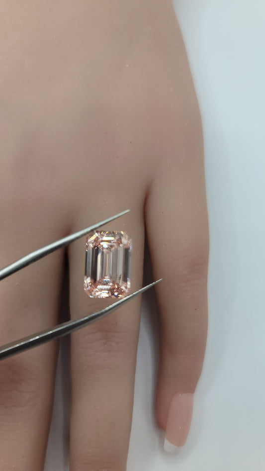 A close-up of a hand holding a rectangular emerald-cut pink lab diamond with metal tweezers against a plain light background.