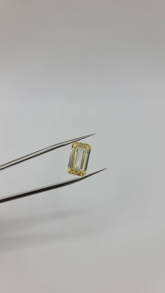 A yellow emerald-cut lab diamond held between metal tweezers against a plain light gray background.