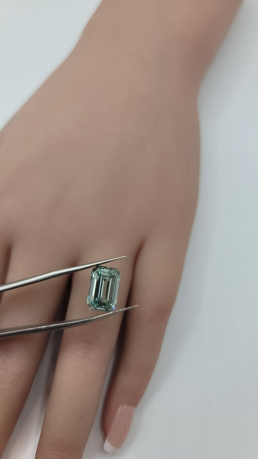 A close-up of a hand holding a rectangular emerald-cut lgreen lab diamond with metal tweezers against a plain light background.