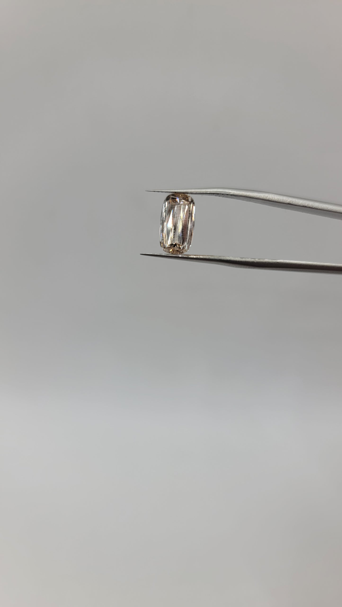 A lab grown crisscut diamond held by metal tweezers against a plain light gray background.